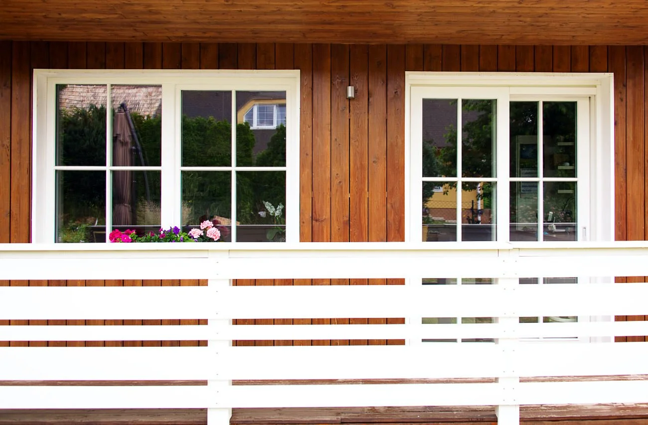 Two white framed windows featuring potted flowers, with white wooden deck railing in front of them