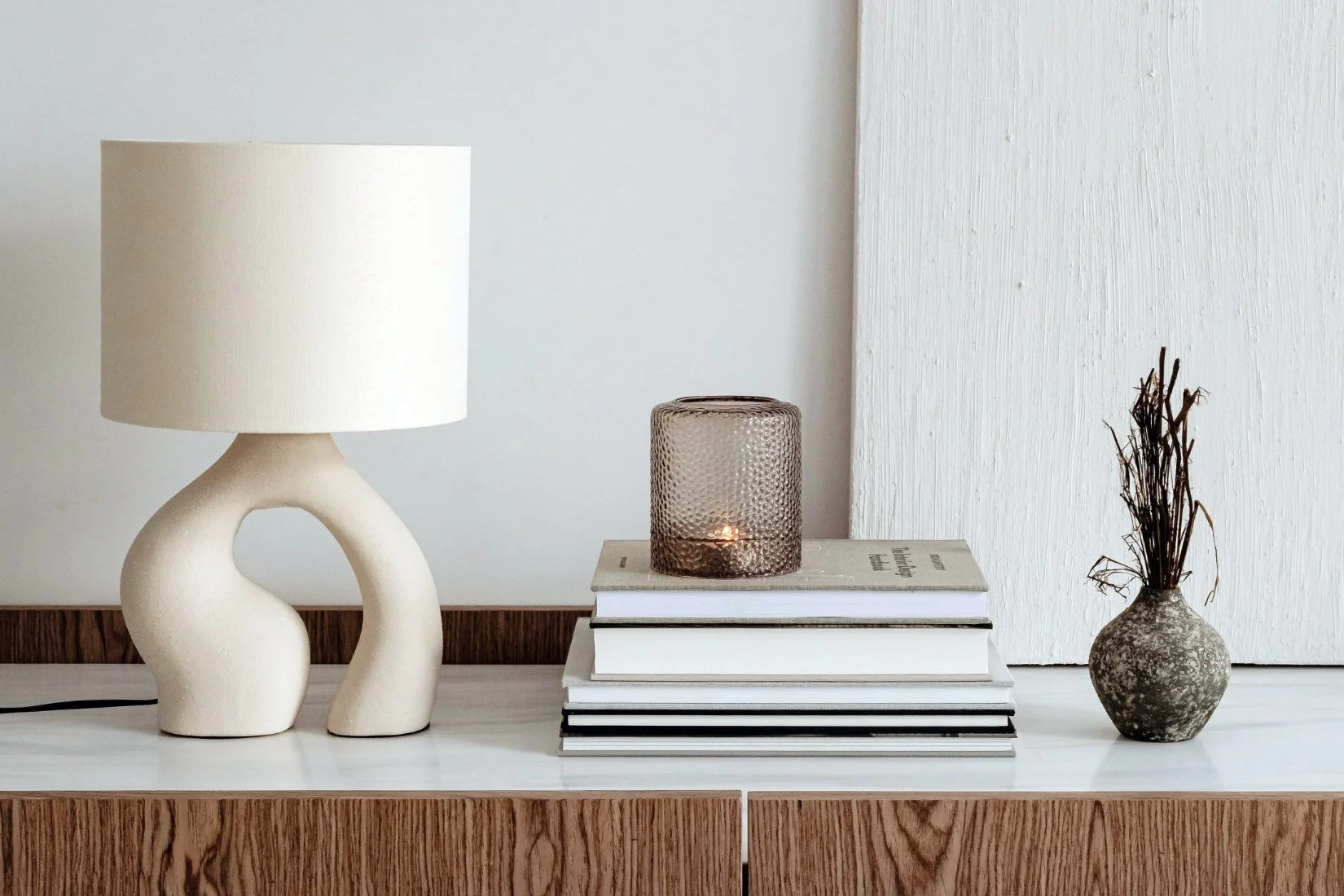 Table lamp with an intricately shaped ceramic base in soft earthy tones, topped with a simple shade.