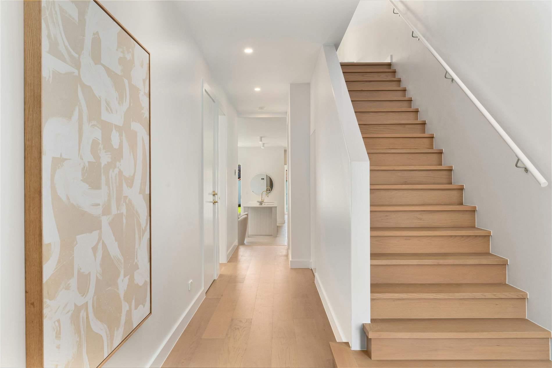 Bright residential transition space design featuring modern timber clad staircase and corridor view into kitchen