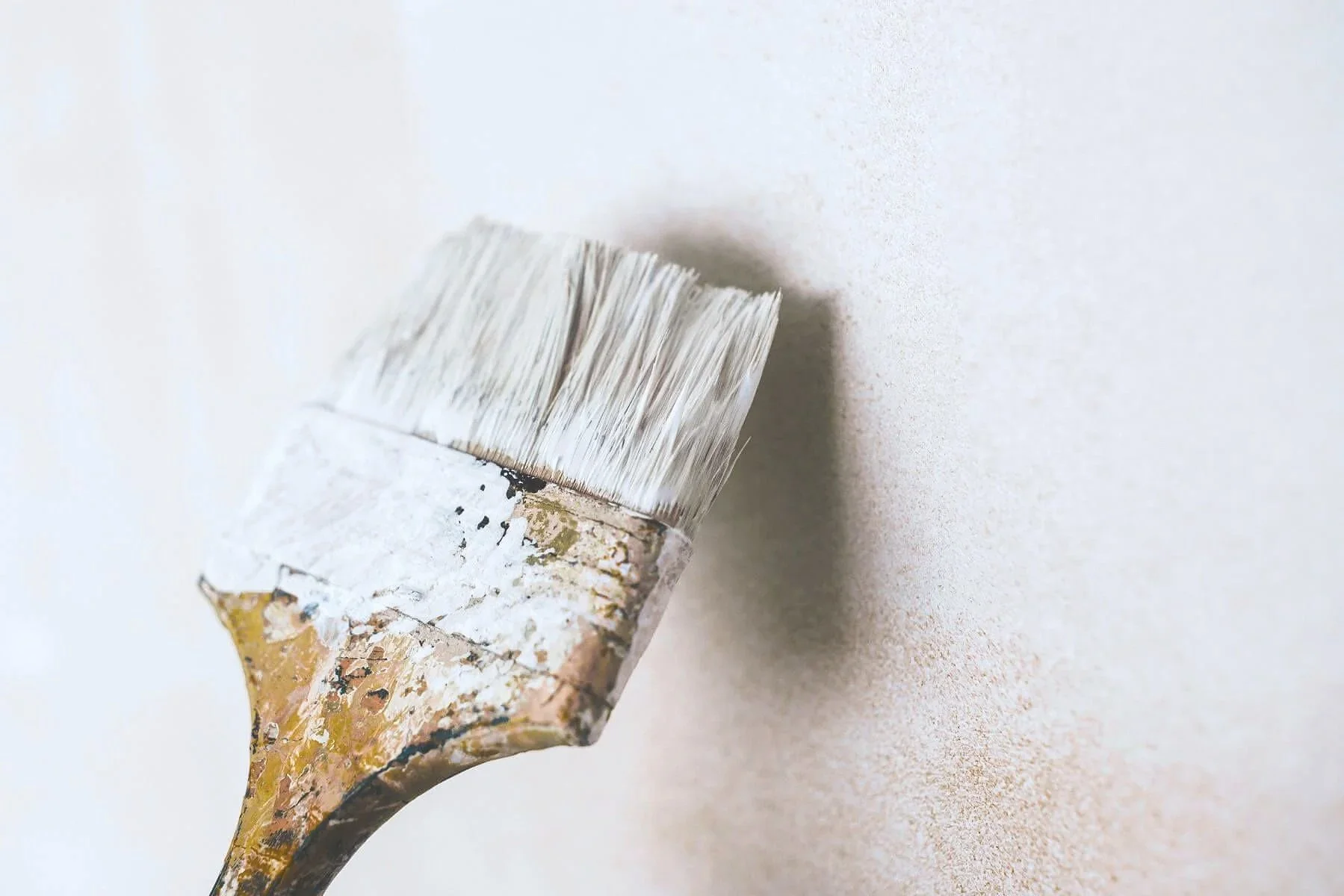 Close-up of a paintbrush applying a coat of eco-friendly wall paint, representing the traditional wall refresh method.