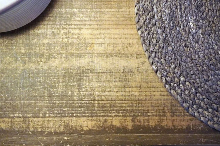 A macro top-down view of a raw wood finish side table styled with a circular textured mat and a minimalist ceramic vase snippet on the left.