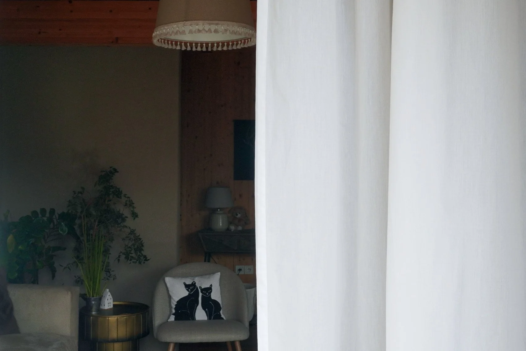 White cotton curtain hanging revealing quiet darker interior behind.