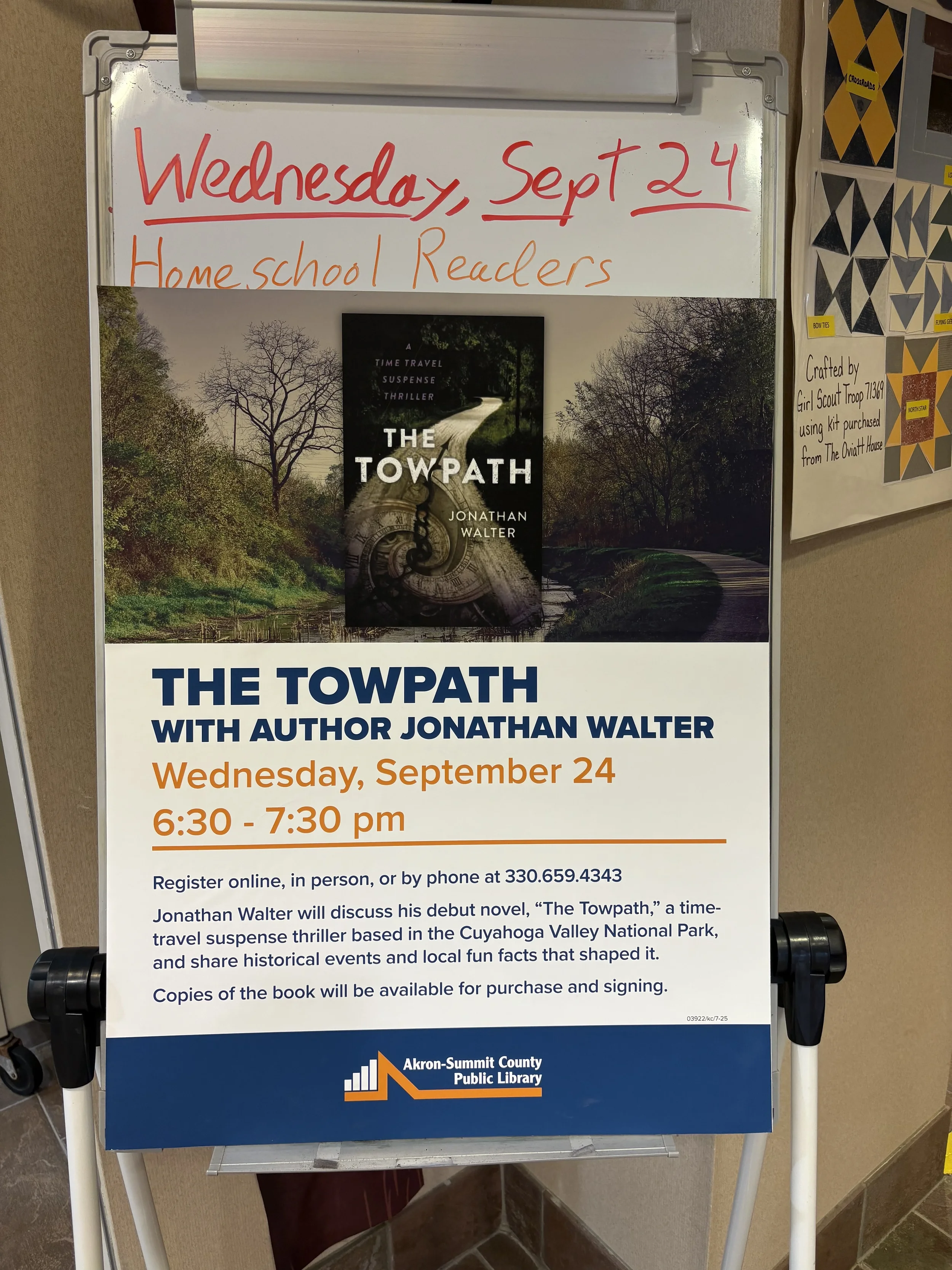 Whiteboard sign advertising a book discussion event for 'The Towpath' by Jonathan Walter, scheduled for September 24 from 6:30 to 7:30 pm at the Akron-Summit County Public Library, with details for registration and purchase.