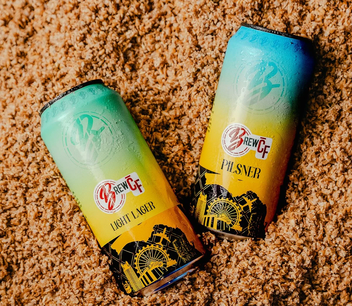 Three cans of craft beer placed on a dark surface, with the front can labeled "Red Lake Ale" depicting a sunset at a lake, and the other two cans slightly blurred in the background.