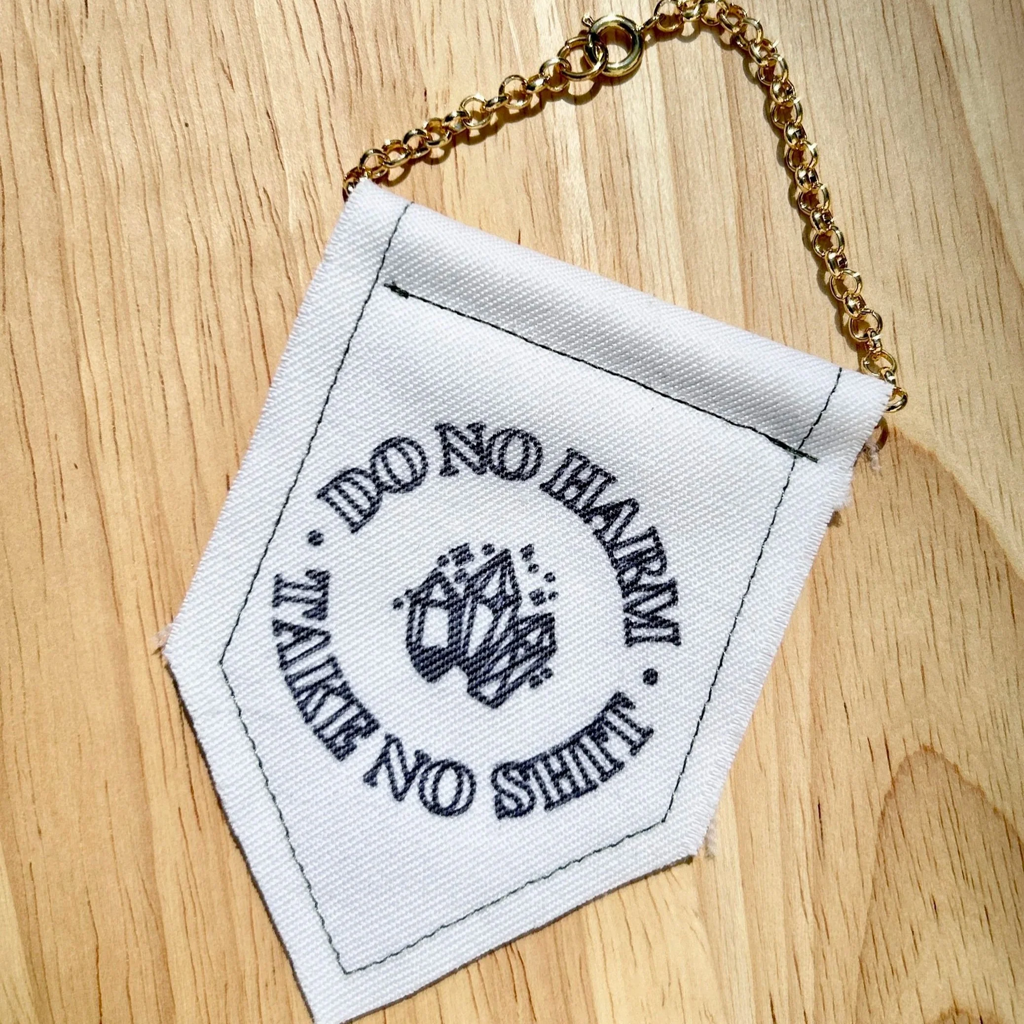 Handmade upcycled white fabric mini banner with "do no harm, take no shit" written in a circle, inside which are three crystals - design is in black infused ink