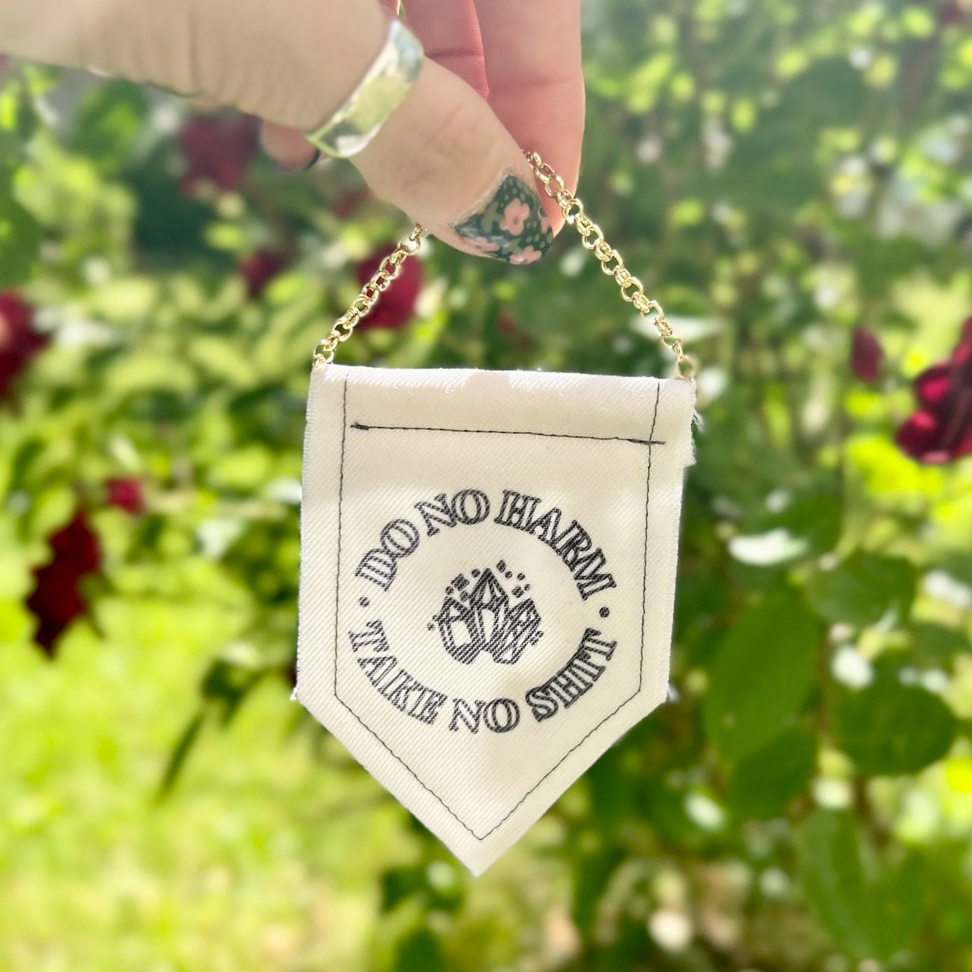 Handmade upcycled white fabric mini banner with "do no harm, take no shit" written in a circle, inside which are three crystals - design is in black infused ink