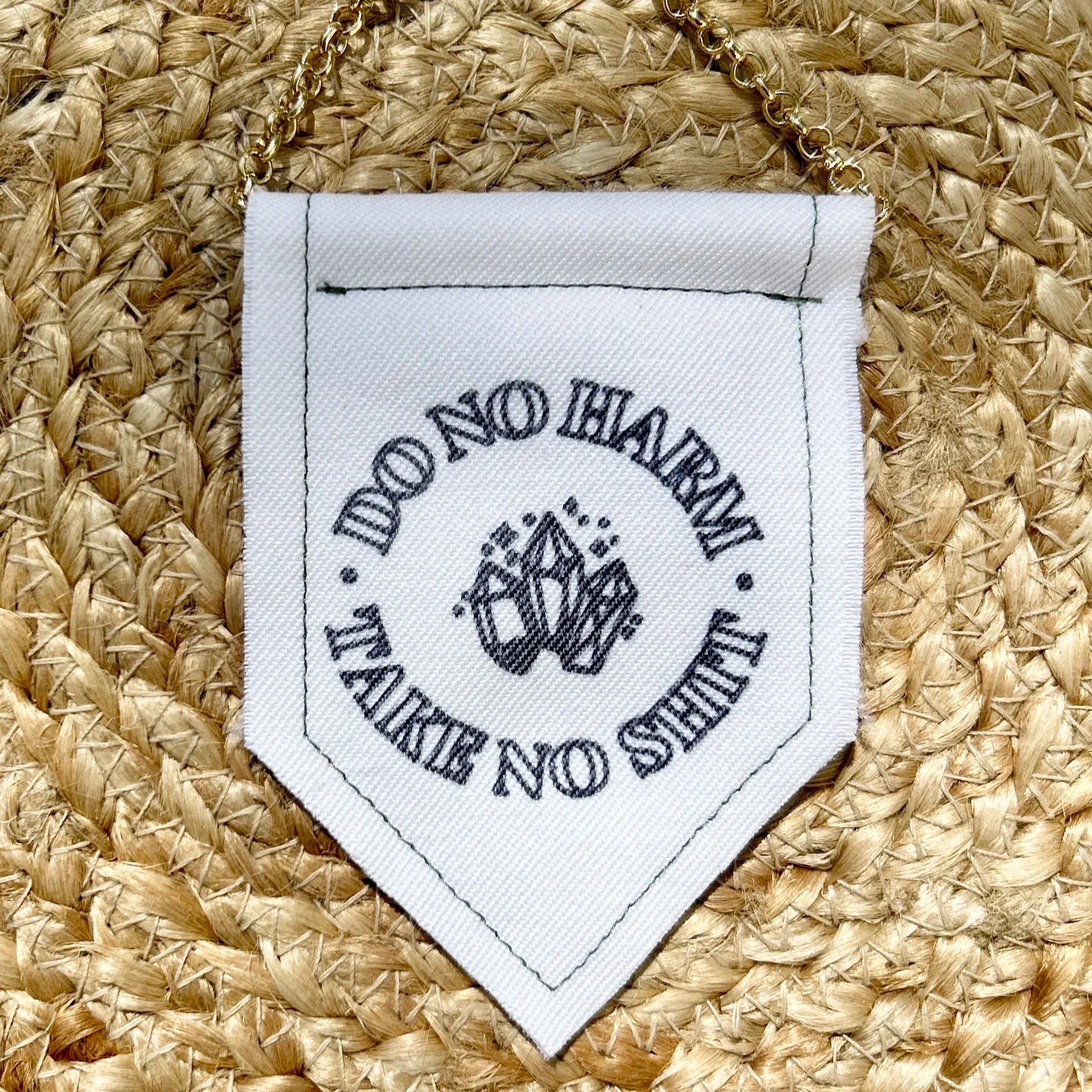 Handmade upcycled white fabric mini banner with "do no harm, take no shit" written in a circle, inside which are three crystals - design is in black infused ink