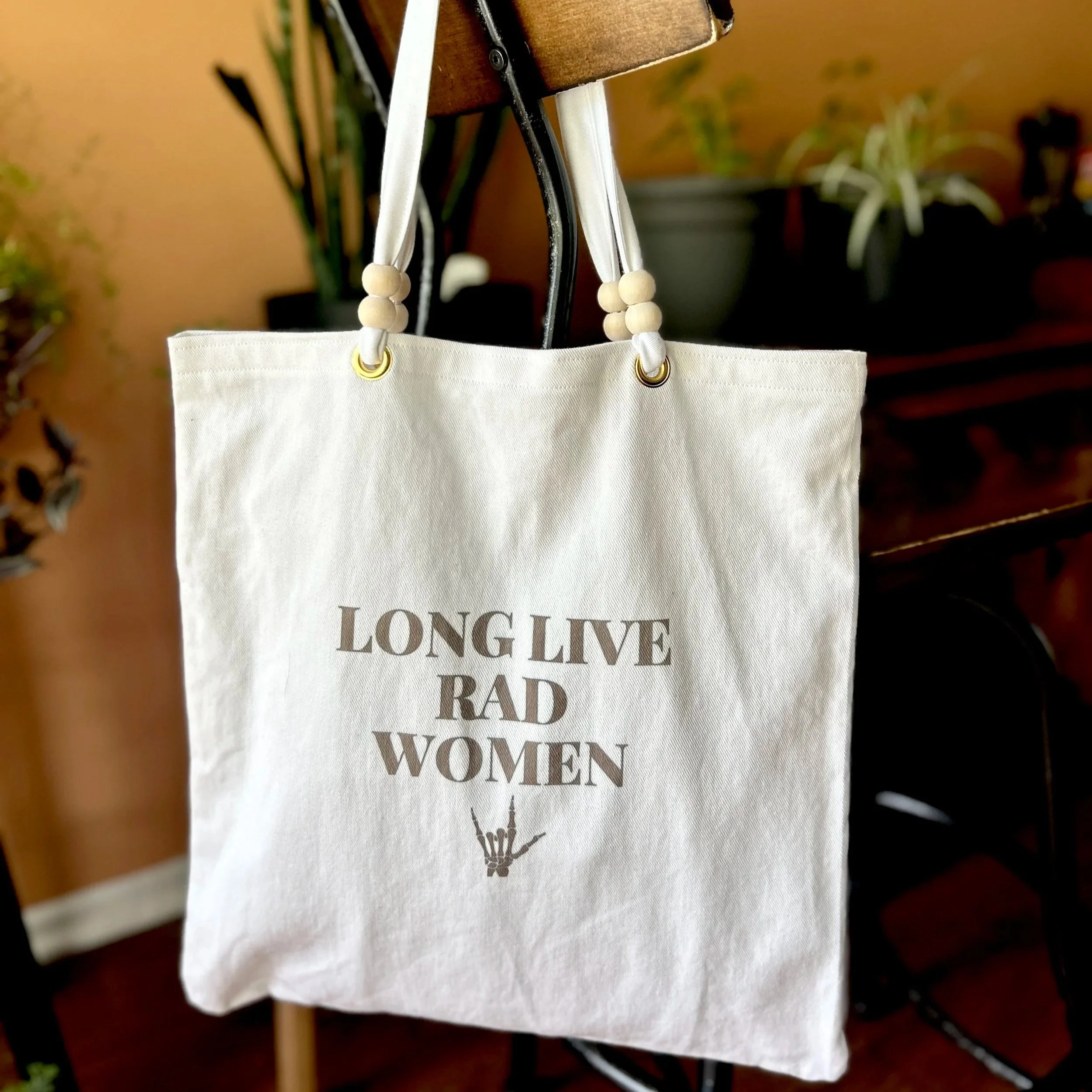 Handmade tote bag made from upcycled off-white curtain canvas featuring a black infused ink design reading 'long live rad women', and wooden bead handle accents.
