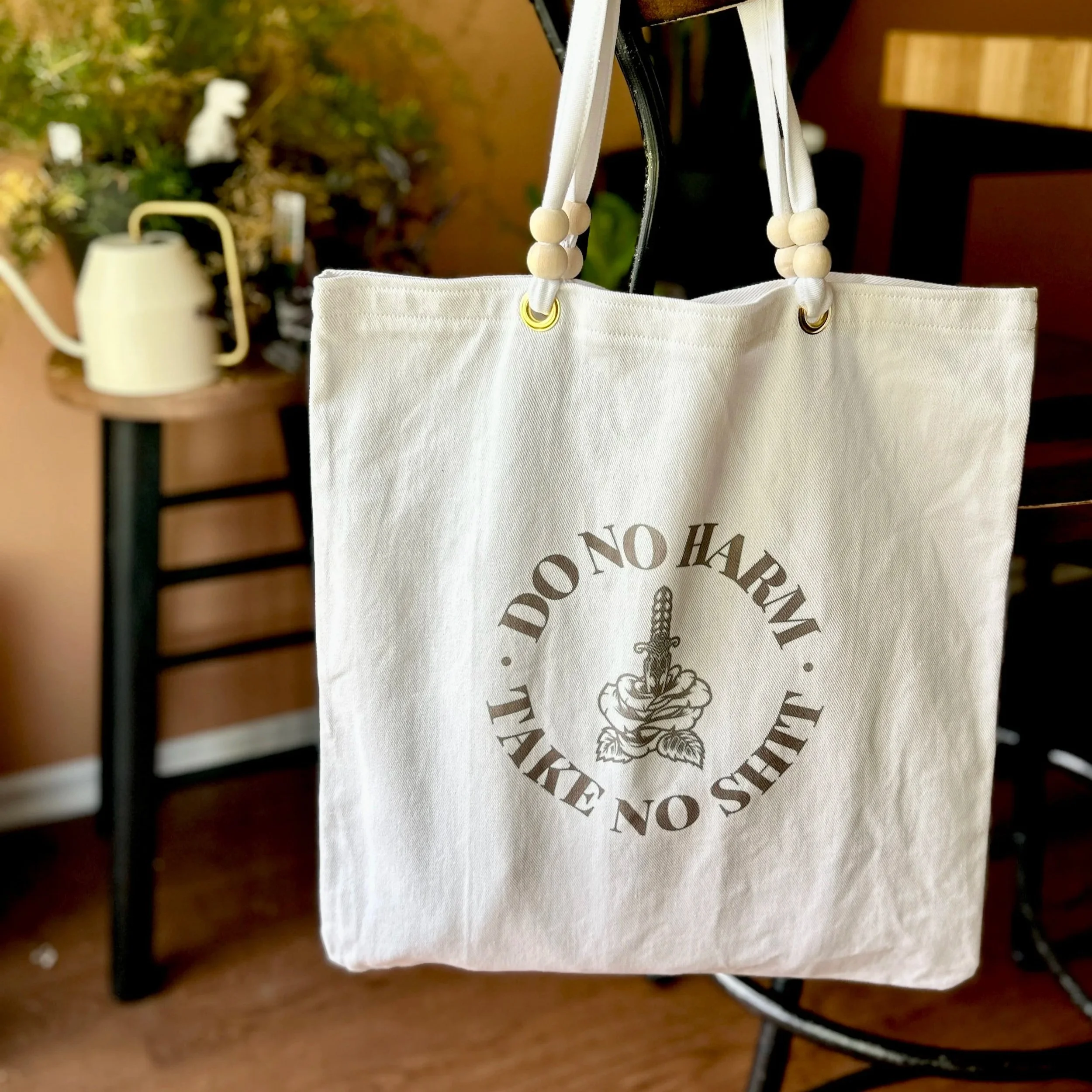 Handmade tote bag made from upcycled off-white curtain canvas featuring a black infused ink design reading 'do no harm, take no shit', and wooden bead handle accents.