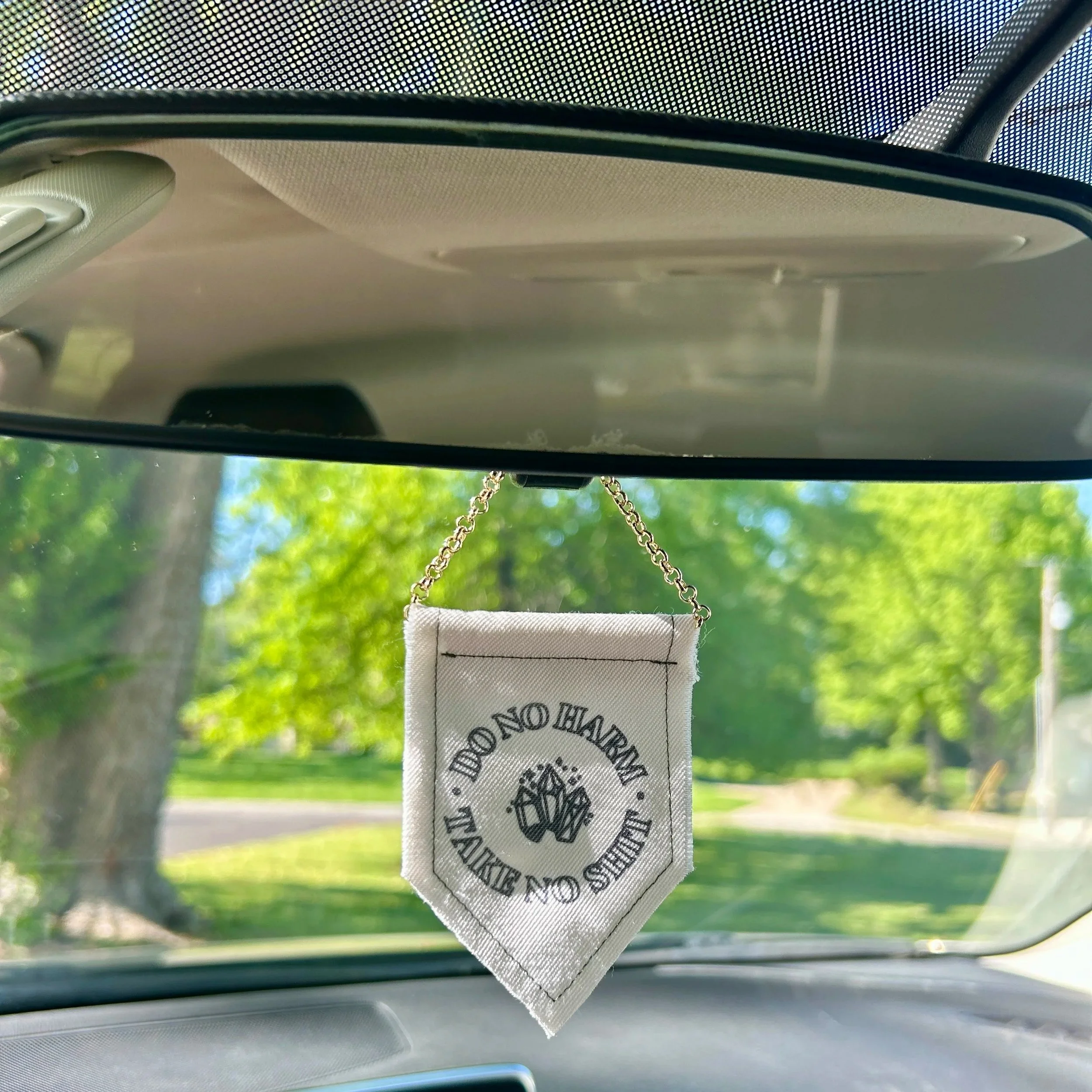 Handmade upcycled white fabric mini banner with "do no harm, take no shit" written in a circle, inside which are three crystals - design is in black infused ink