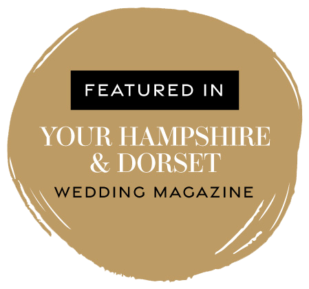 A circular logo with a gold brushstroke background, featuring text that says 'Featured in Your Hampshire & Dorset Wedding Magazine'.