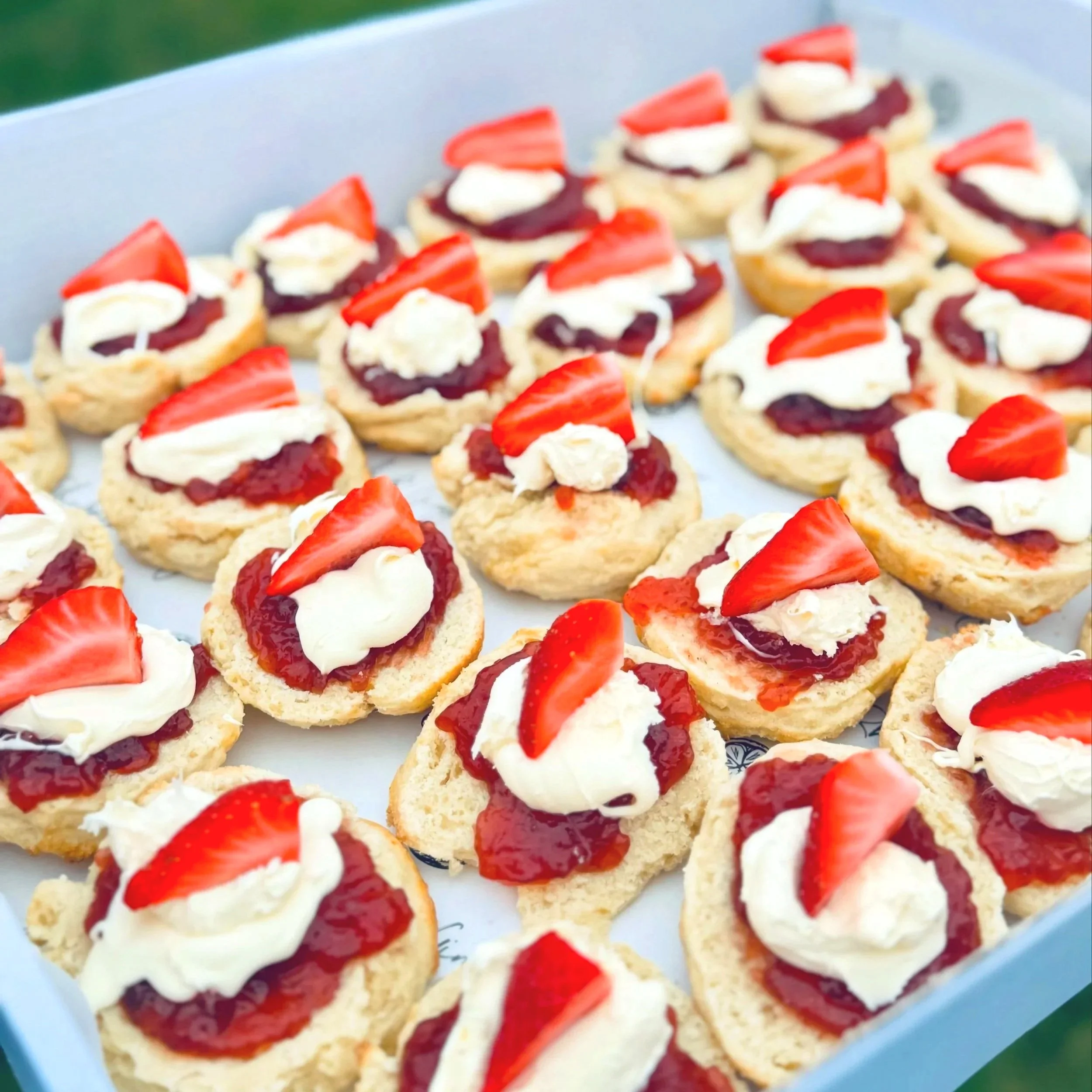 Assorted strawberry shortcake bites topped with whipped cream and fresh strawberry slices, arranged on a tray.