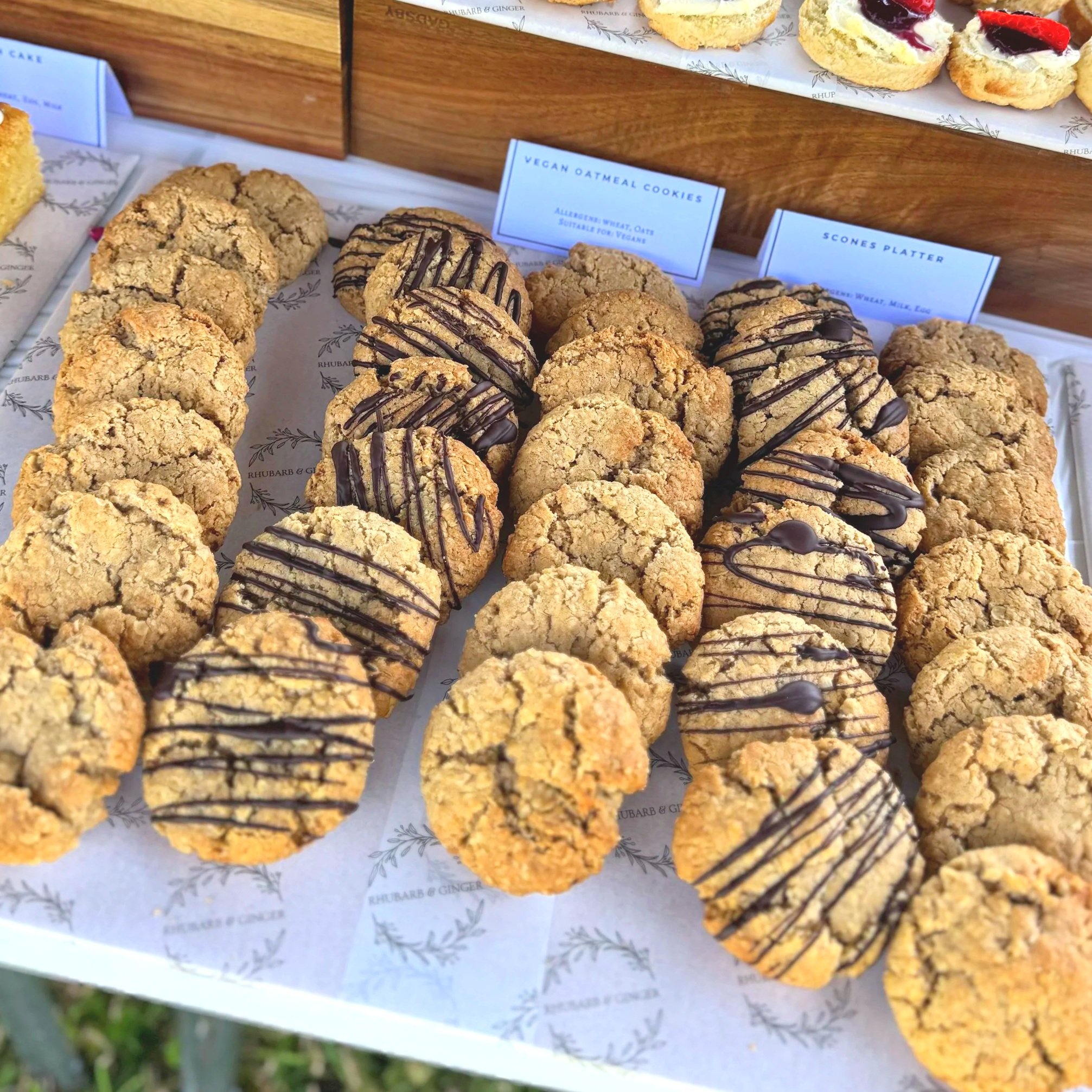 Variety of cookies displayed on a tray, including vegan oatmeal cookies and scones platter, some drizzled with chocolate.