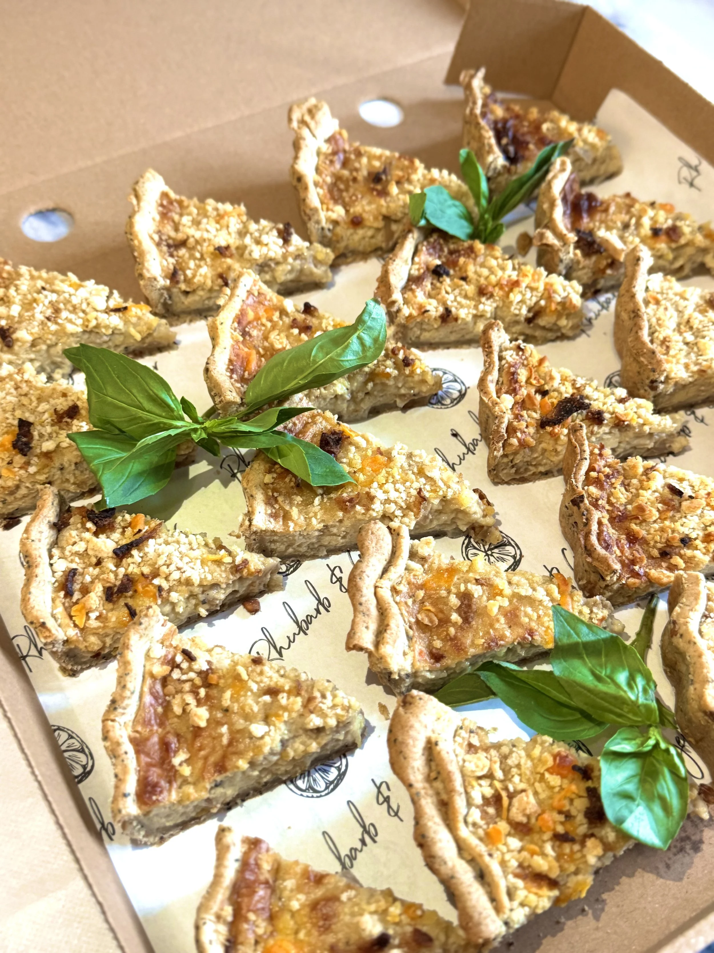 A box of triangular fruit crumble bars garnished with fresh basil leaves.