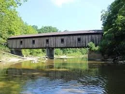 North Kingsville covered bridge spanning a creek with trees along the shoreline on a sunny day.