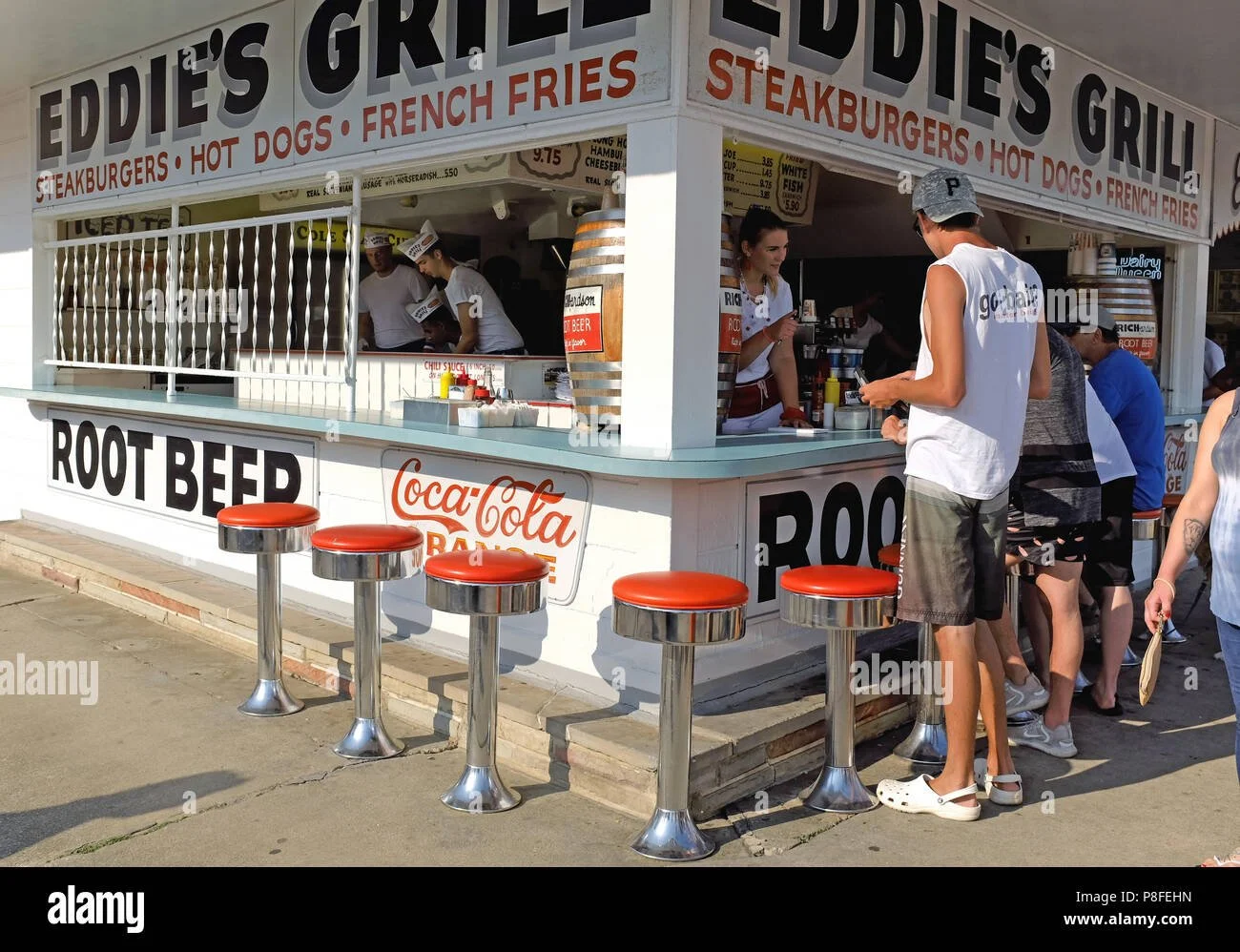 Eddie’s Grill food stand on the Geneva-on-the-Lake boardwalk with “Root Beer” signage, red counter stools, and customers ordering at the window.