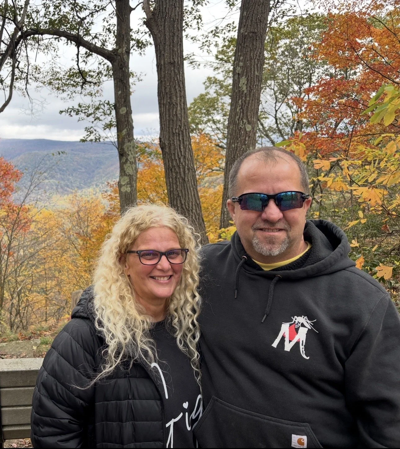 Owners of Mosquito Assassin Pest Control standing together outdoors during fall, wearing company apparel with autumn trees in the background.
