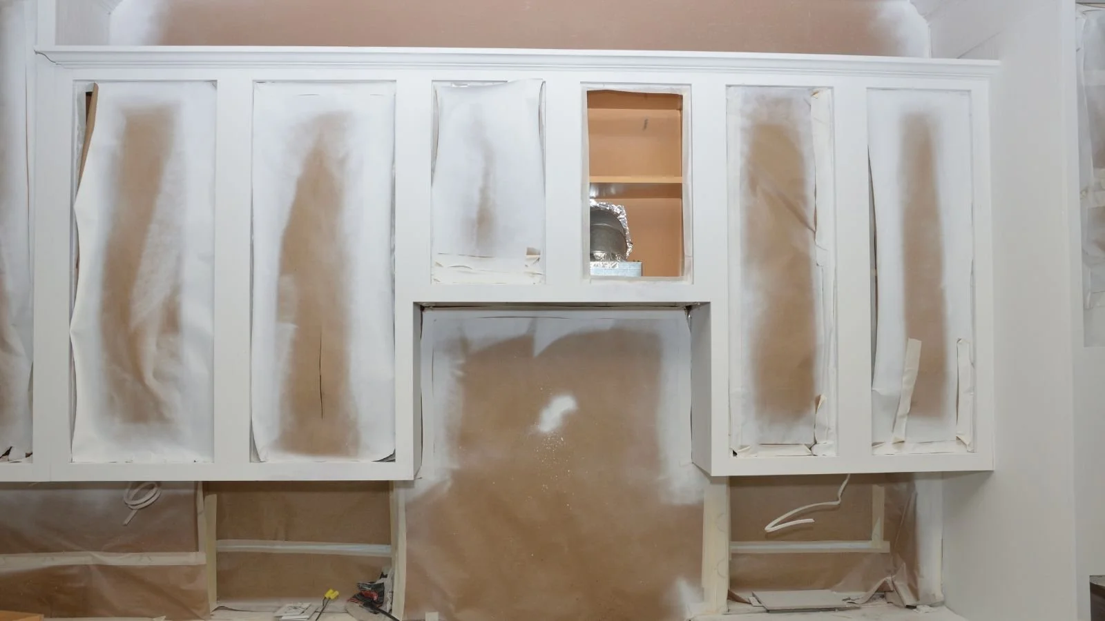 Partially installed white kitchen cabinets against a wall with drywall and construction materials