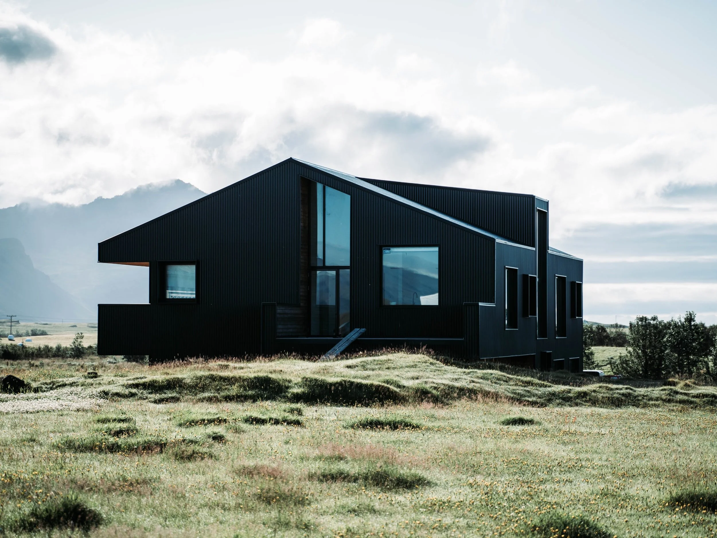 Modern black house in green landscape with cloudy mountain background.