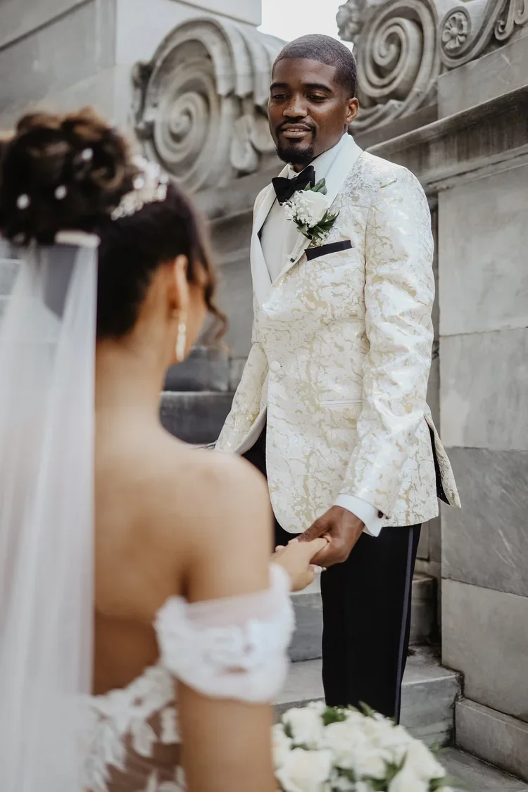 Bride and groom holding hands during their wedding ceremony outside a stone building with ornate architectural details.