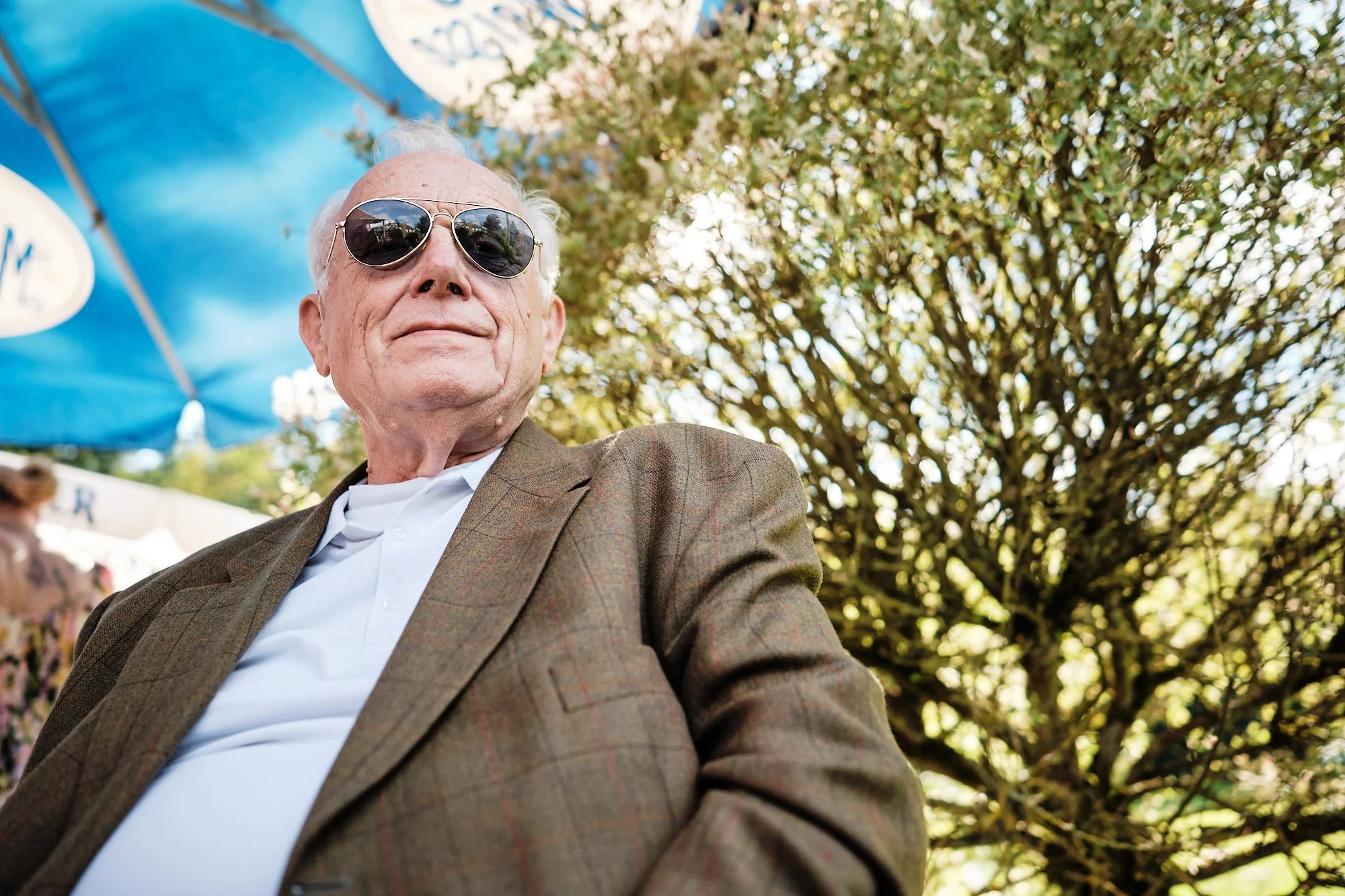 Portrait eines älteren Mannes bei einer Hochzeit, lässig im Tweed-Blazer mit Sonnenbrille, coole Anmutung.