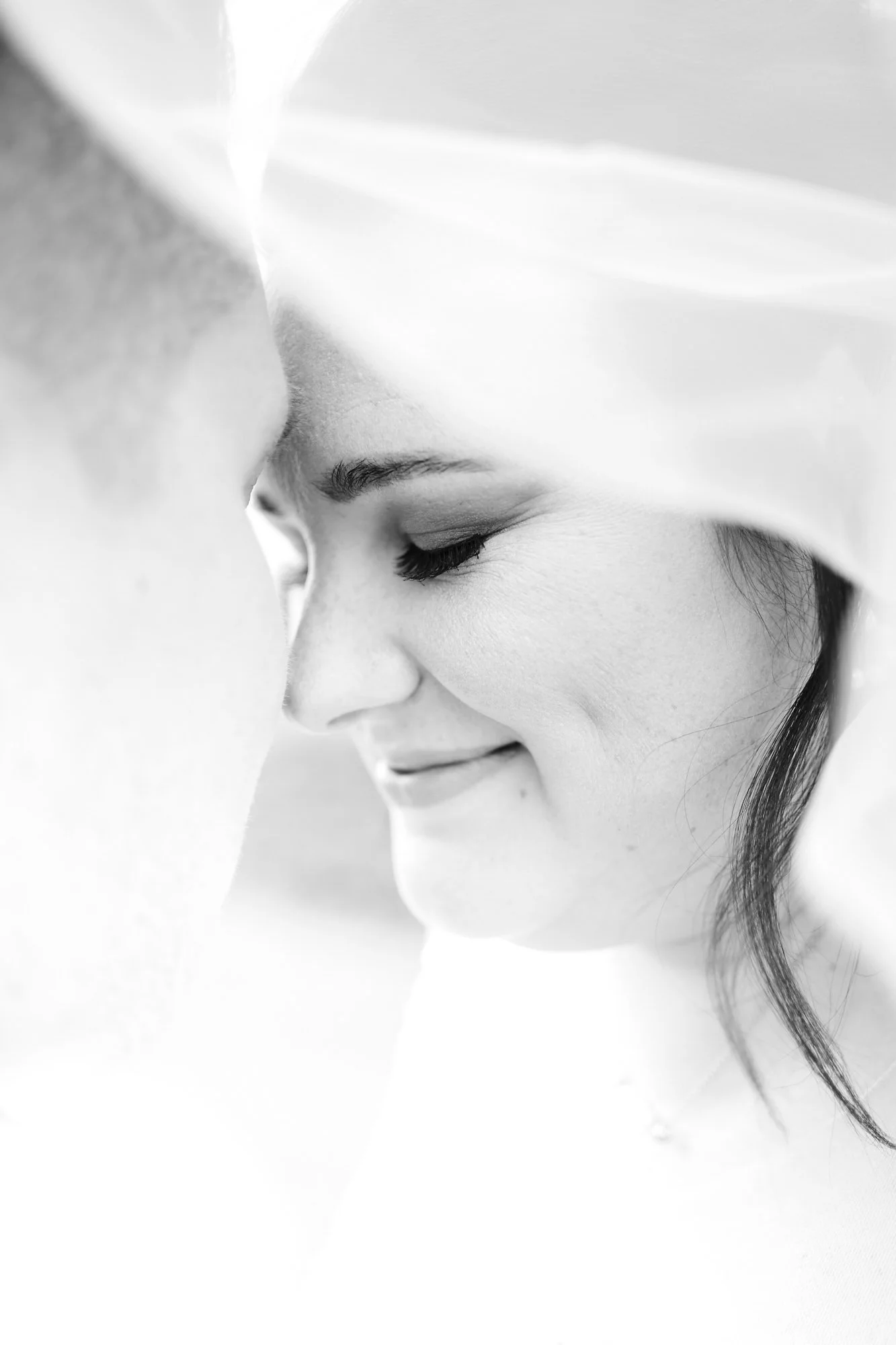 Ruhiges, nahes Schwarz-Weiß-Porträt einer Braut mit Schleier, sanftes Lächeln und geschlossenen Augen.