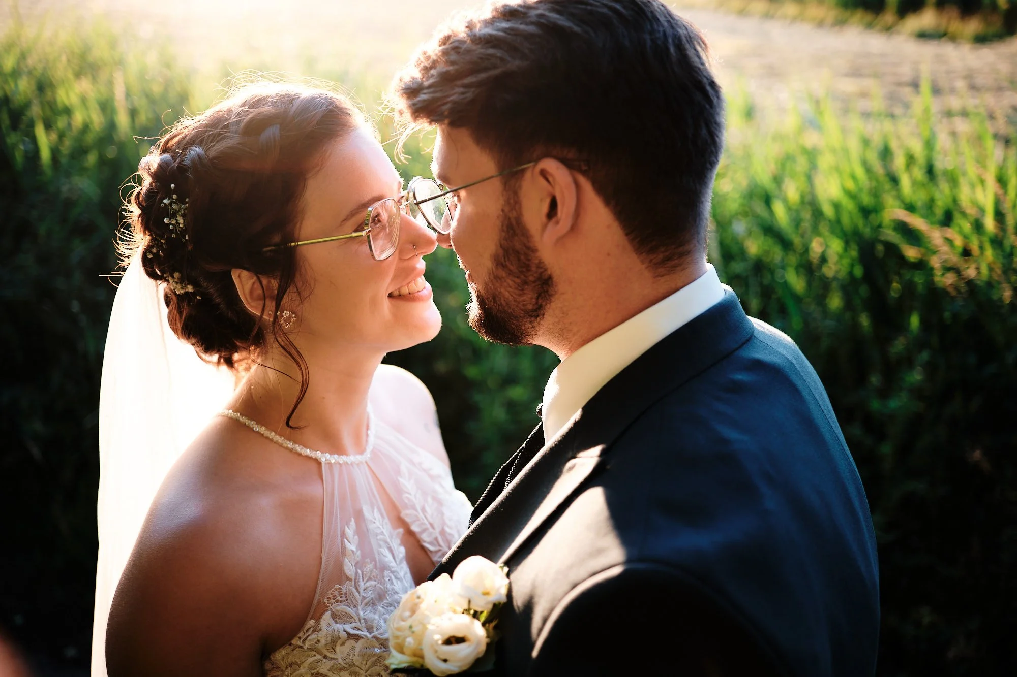Ein Brautpaar bei Sonnenuntergang, das sich gegenübersteht und sich liebevoll anblickt, mit grüner Natur im Hintergrund.