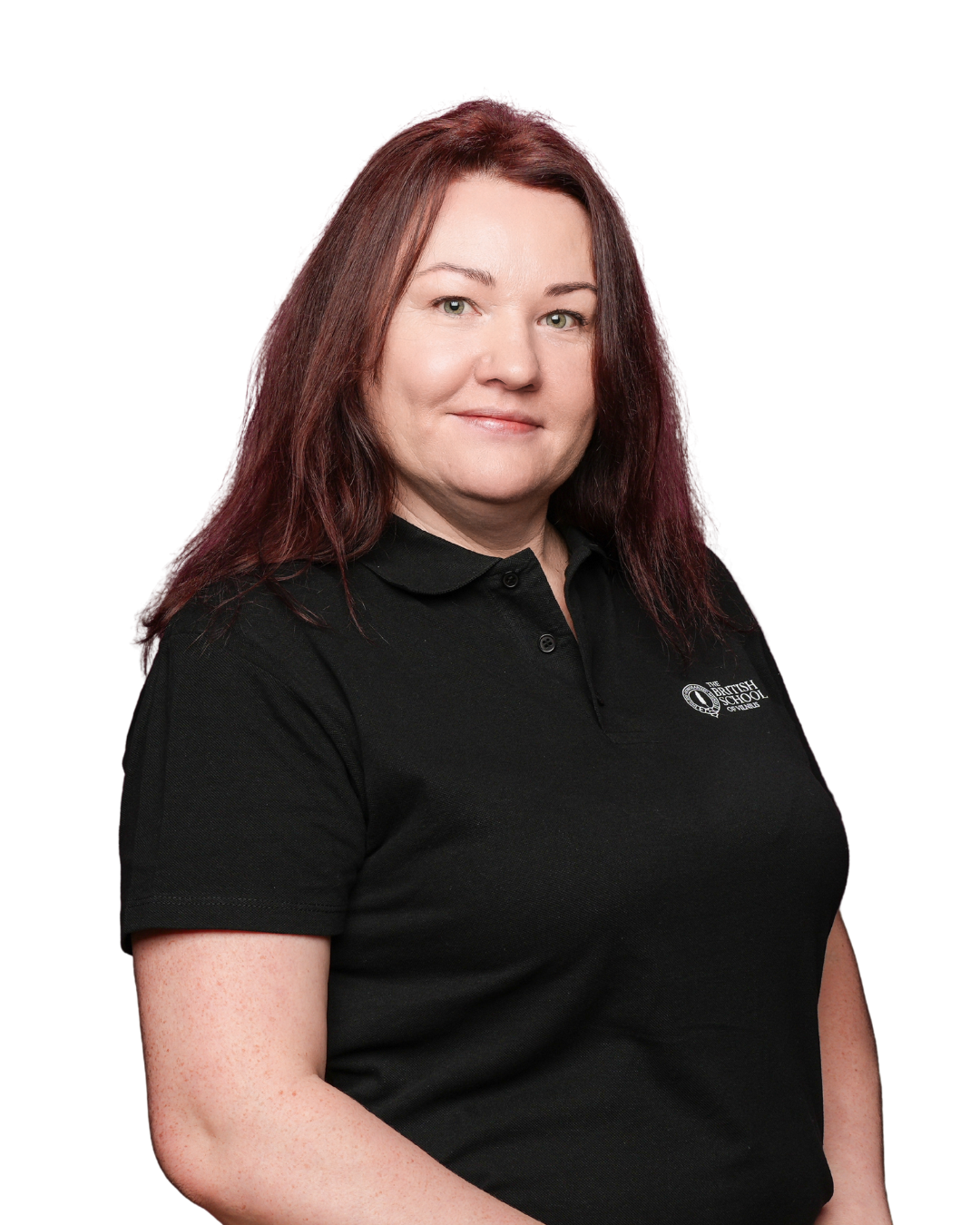 A woman with dark brown hair, fair skin, and blue eyes wearing a light blue polo shirt that has a logo on the chest, standing against a plain background.