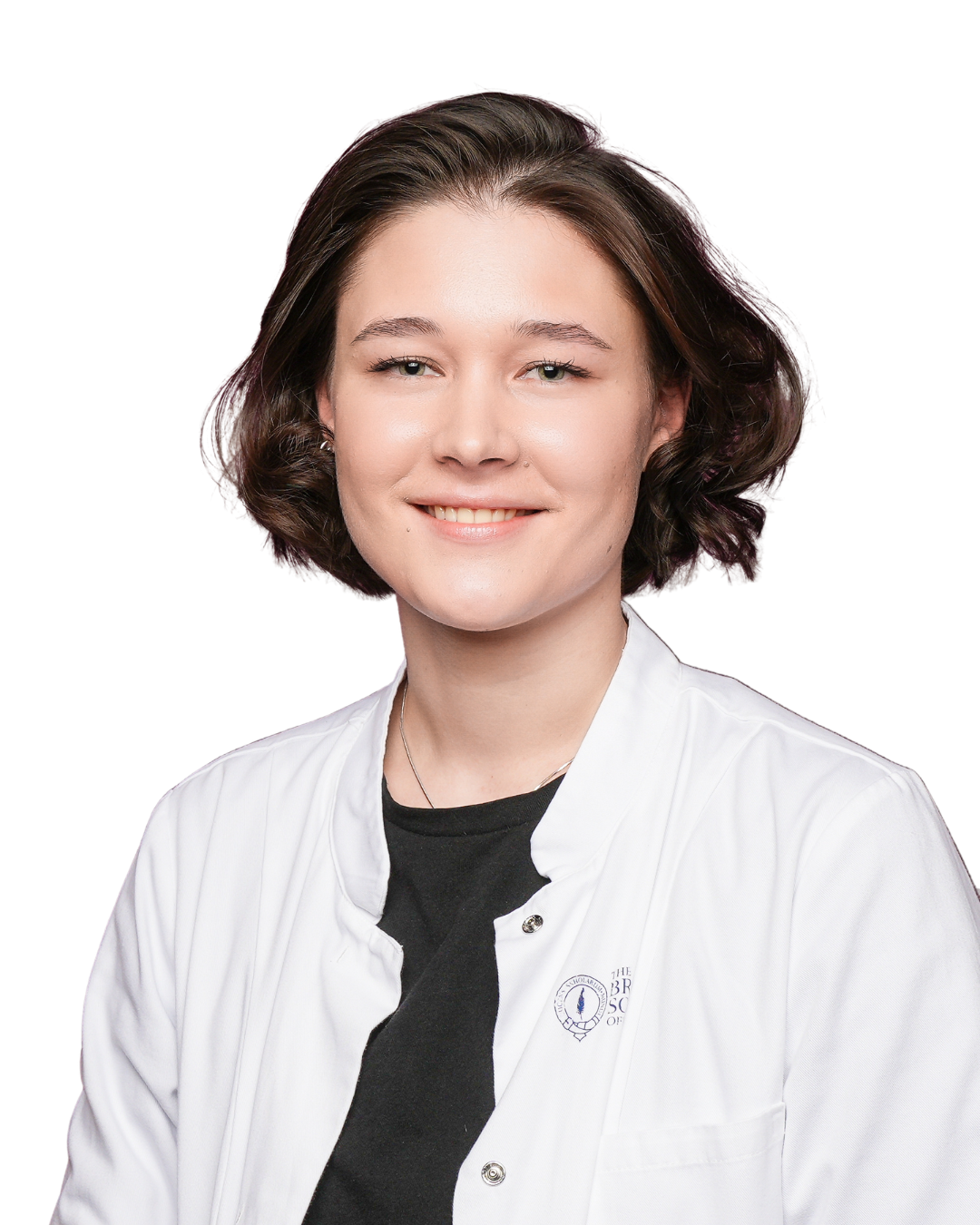 A young woman with shoulder-length dark brown hair wearing a black blazer and T-shirt, standing against a plain white wall.