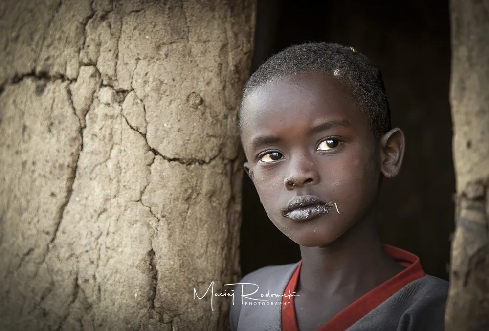 young boy in grey tee shirt looking from doorway in Tanzania
