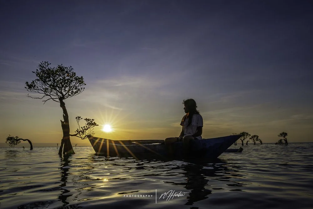 Girl in boat and dancing trees at sunset in Sumba
