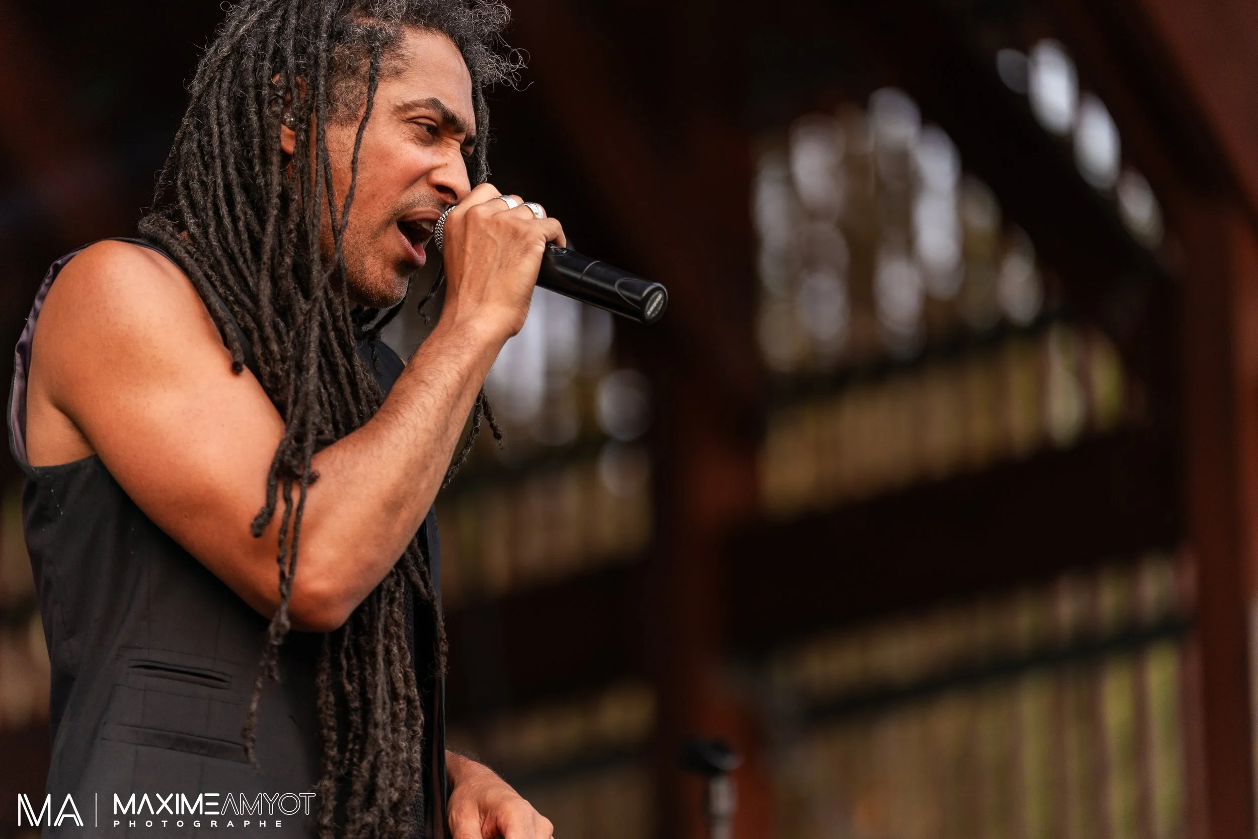 Homme avec dreads chantant dans un micro lors d'une performance musicale.