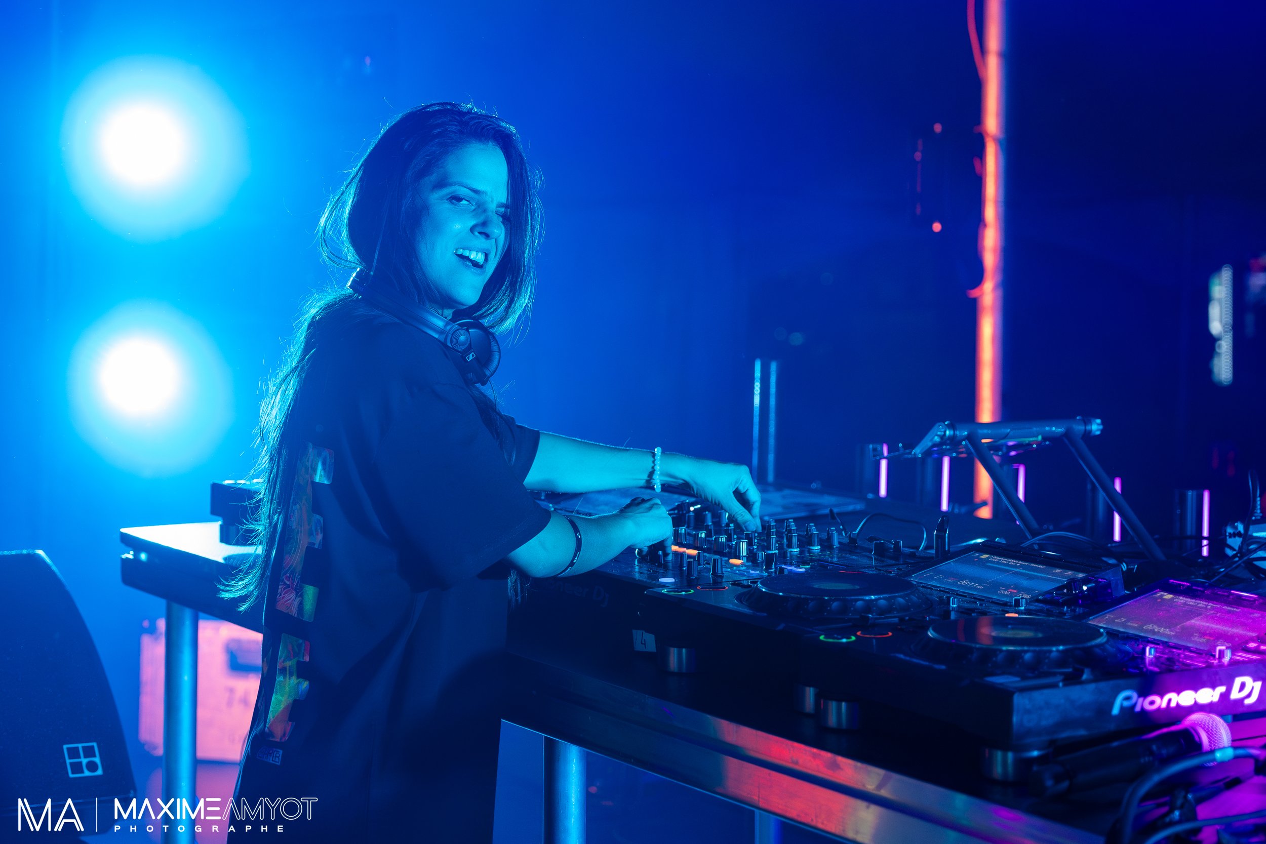 DJ femme jouant de la musique dans un club avec éclairage bleu et violet, utilisant un plateau de mixage Pioneer DJ.