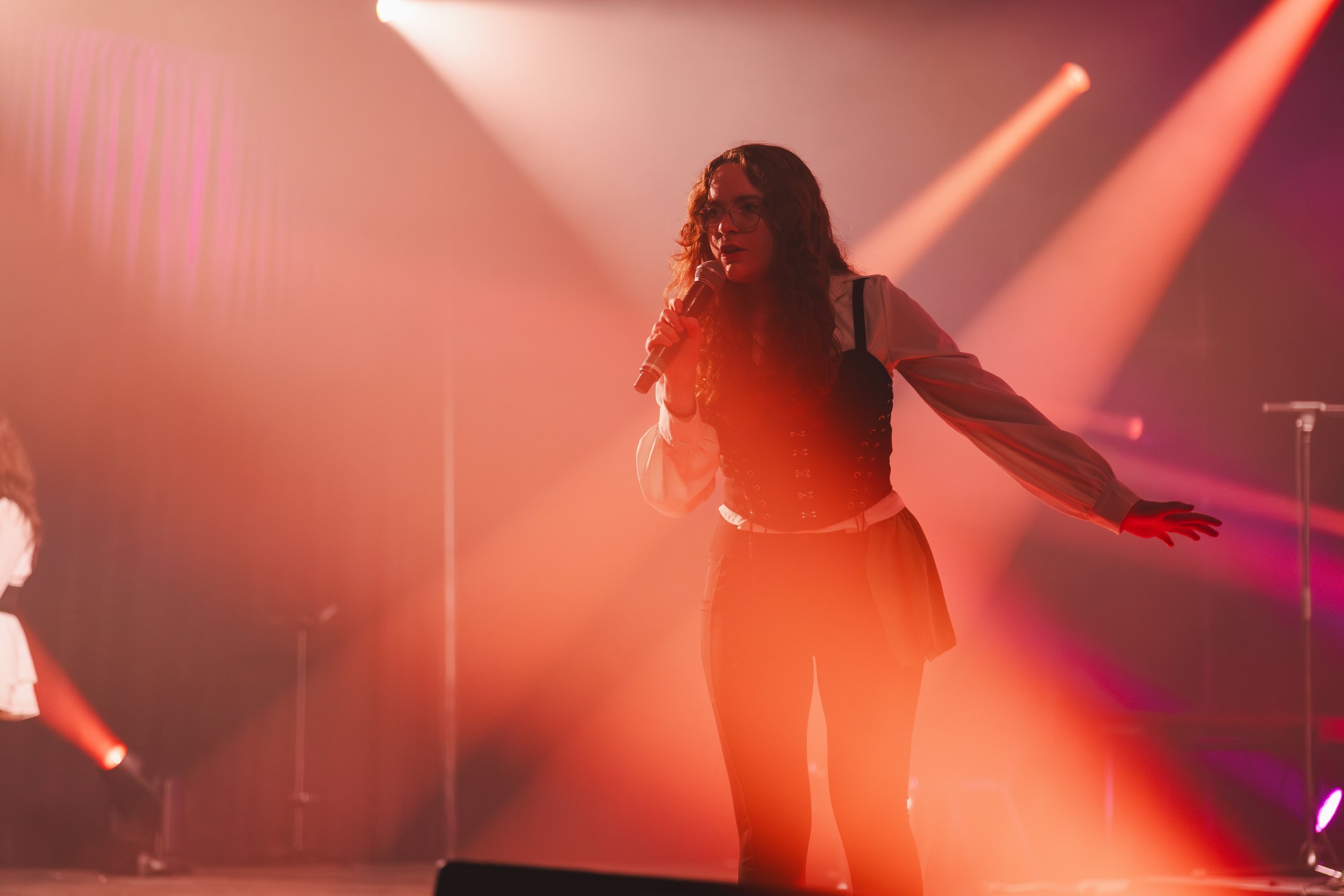 Une femme chante avec un microphone sur scène, éclairée par des lumières colorées et de la vapeur ou du brouillard
