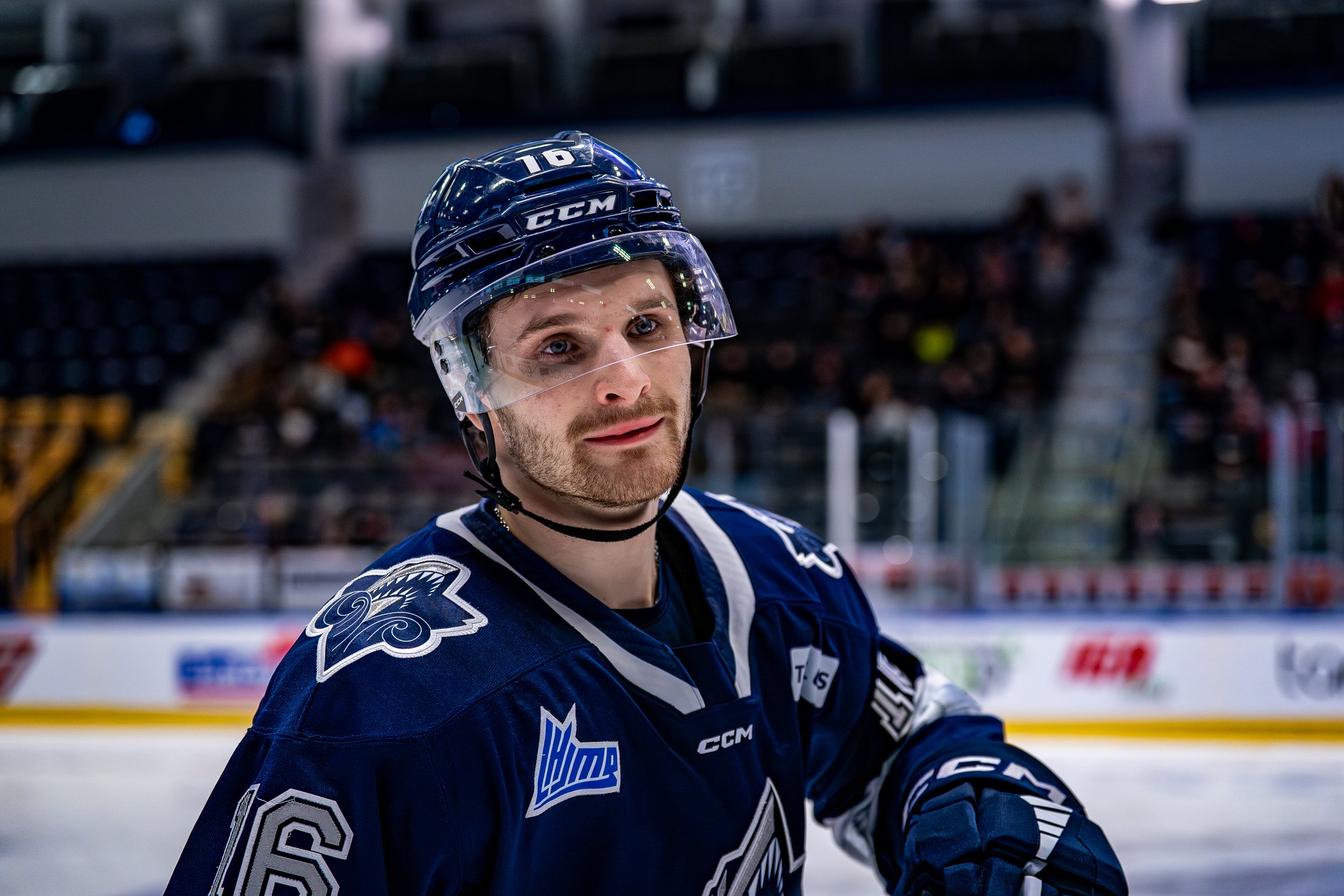Un joueur de hockey sur glace portant un casque et un uniforme bleu, sur la glace lors d'un match.
