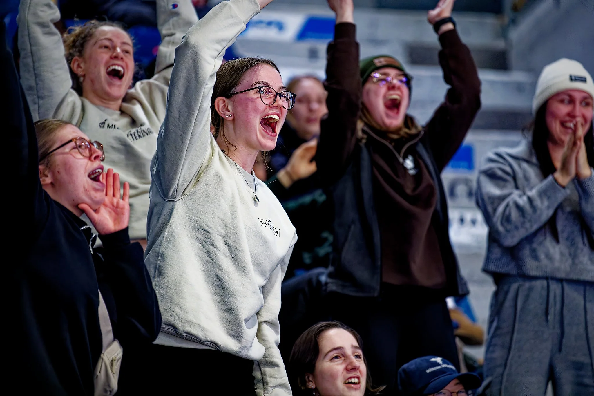 Group of women at a sports event cheering and celebrating, some with arms raised and smiling.