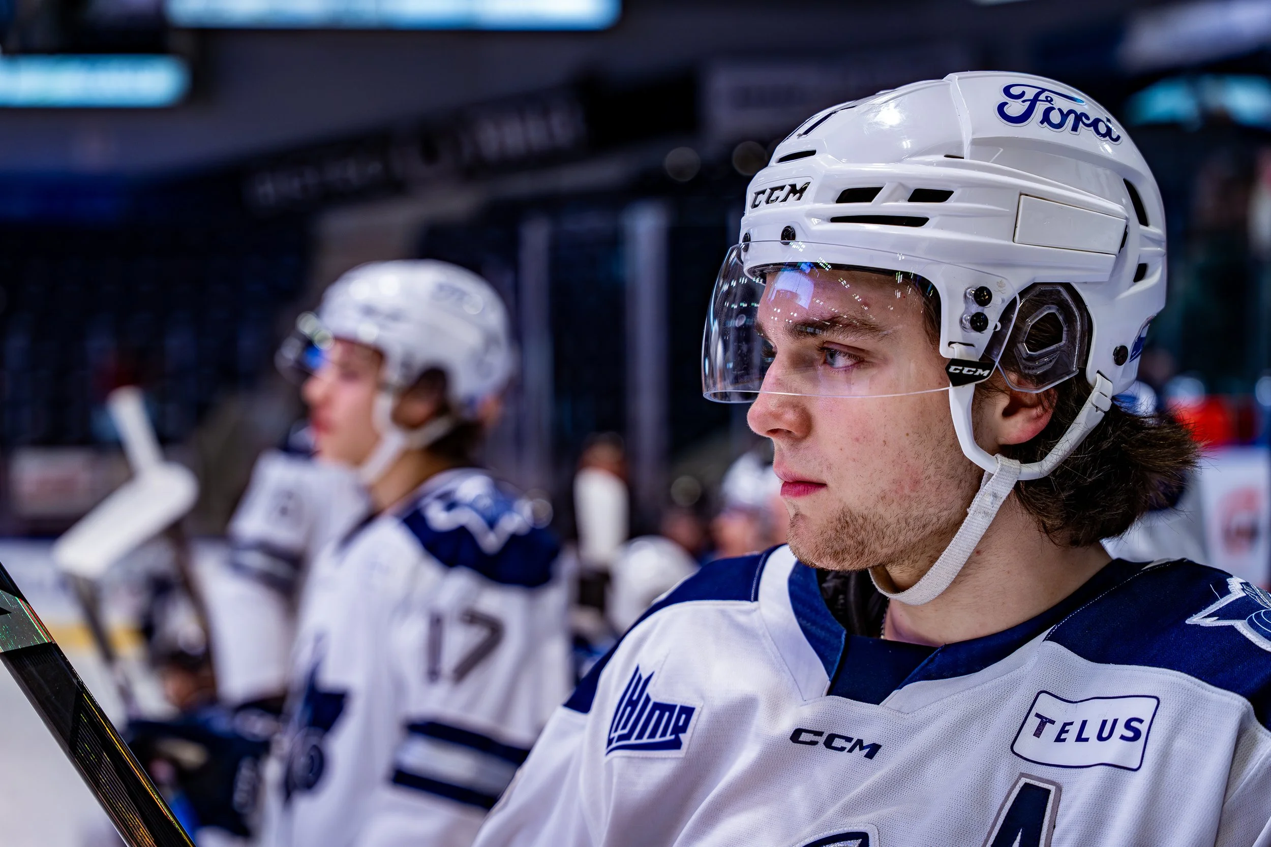 Joueur de hockey sur glace portant un casque et un uniforme avec le logo Ford, en position de concentration, sur le banc.”}