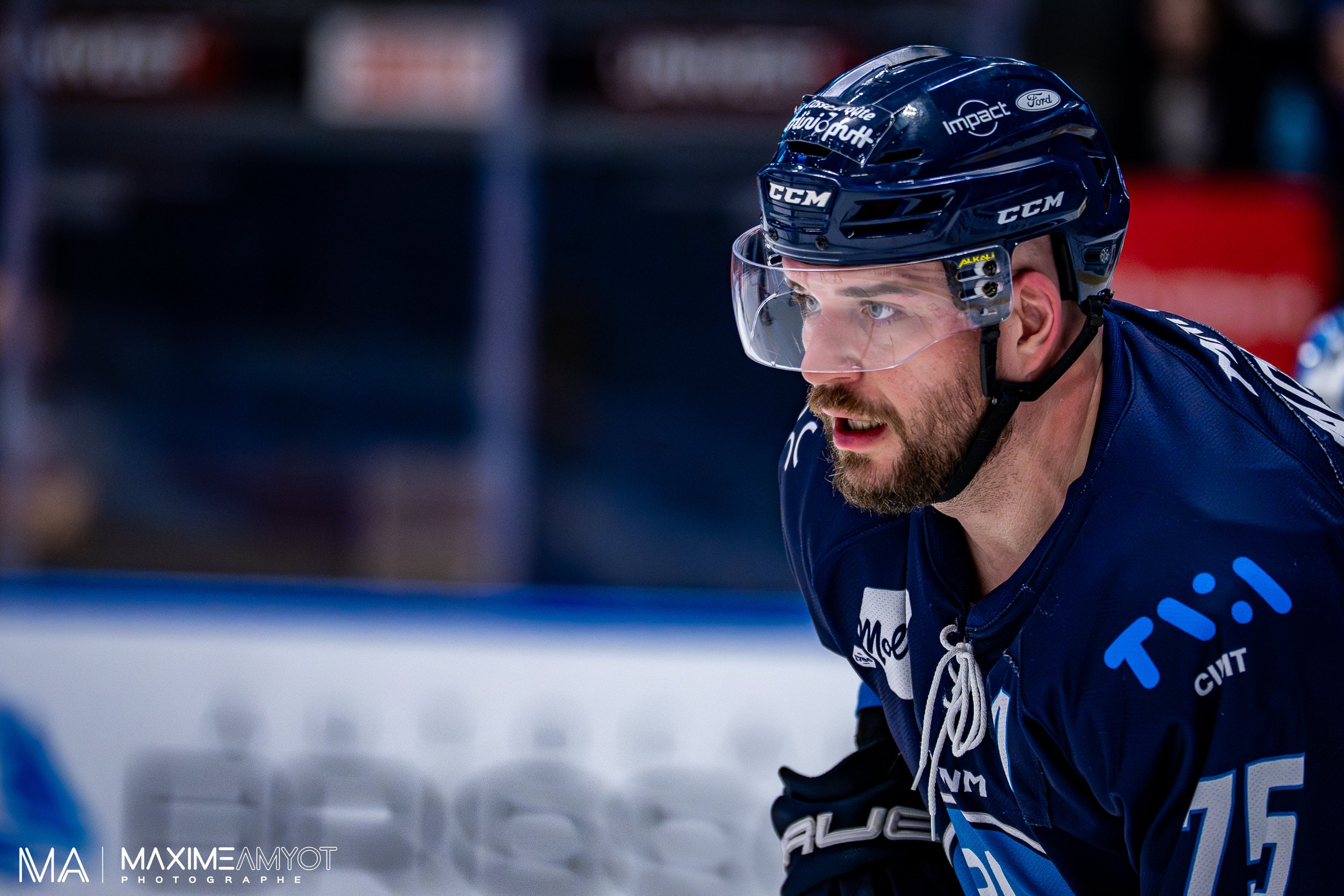 Un joueur de hockey sur glace en tenue bleue avec un casque et un visière, concentré pendant un match.