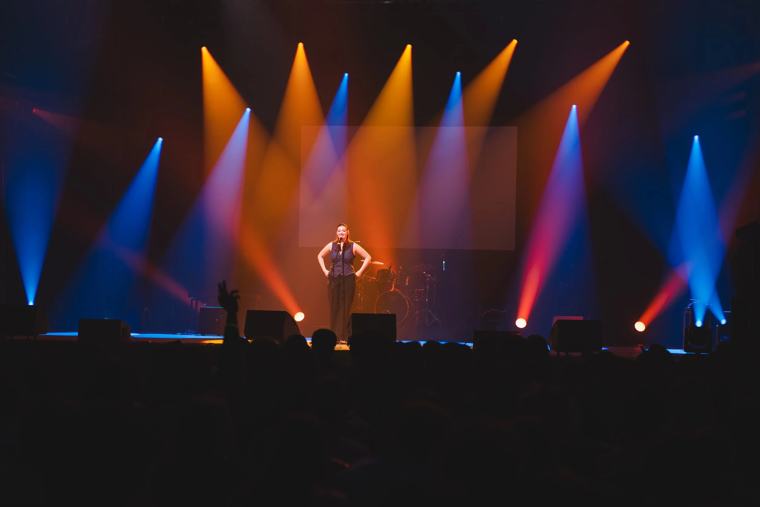 Une chanteuse se produit sur scène avec des lumières colorées en arrière-plan, dans une salle de concert sombre.