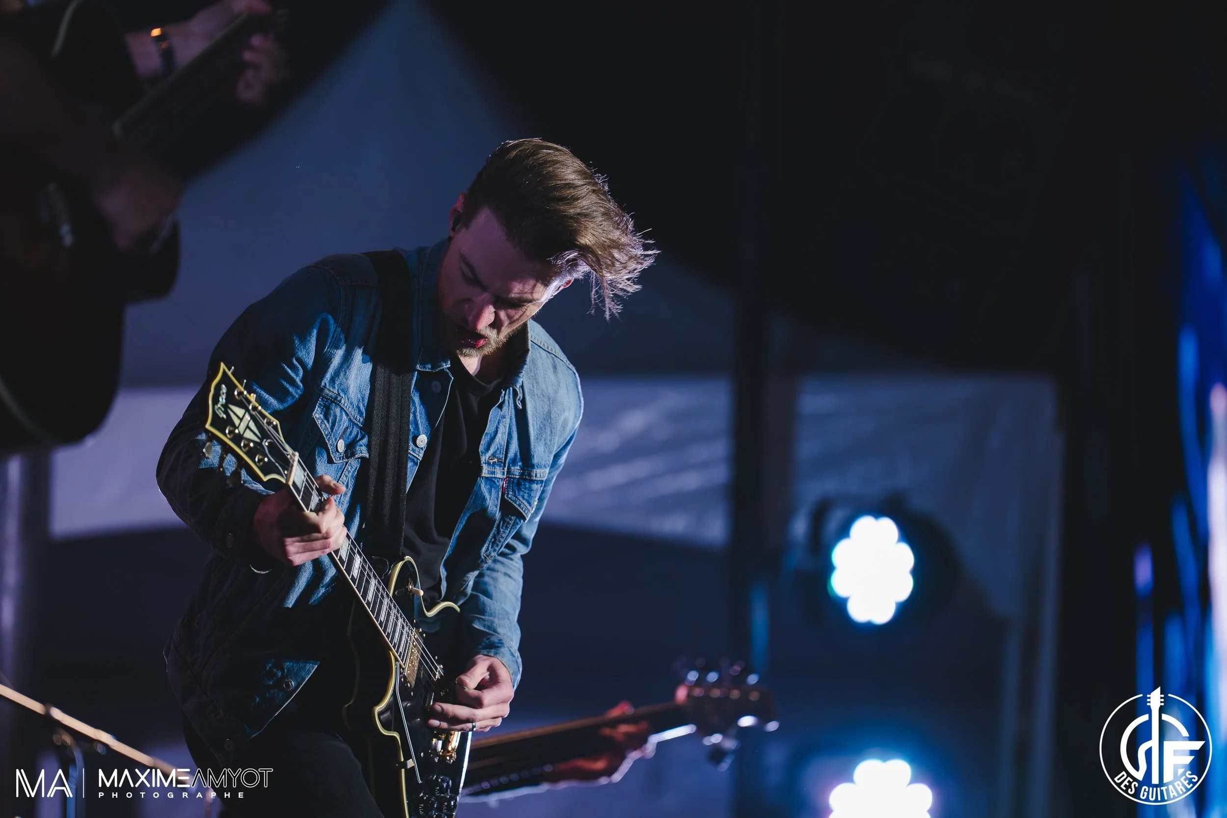 Musicien jouant guitare électrique lors d'un concert, éclairage de scène bleu.