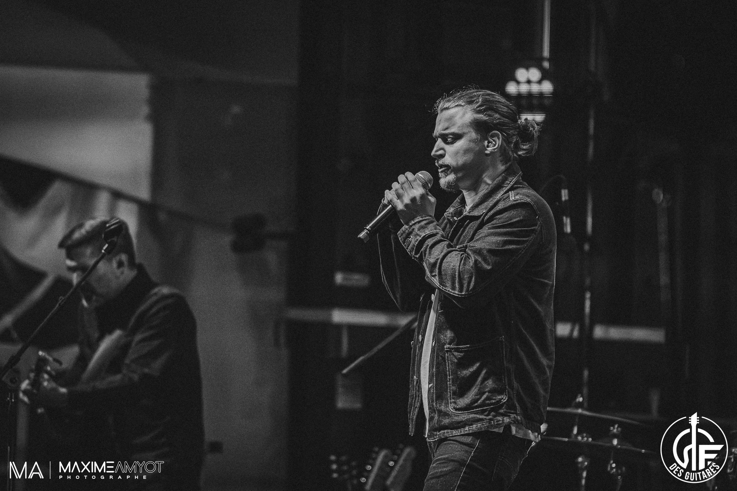 Deux musiciens en concert, un chanteur avec un micro et un guitariste, en noir et blanc, sur scène.