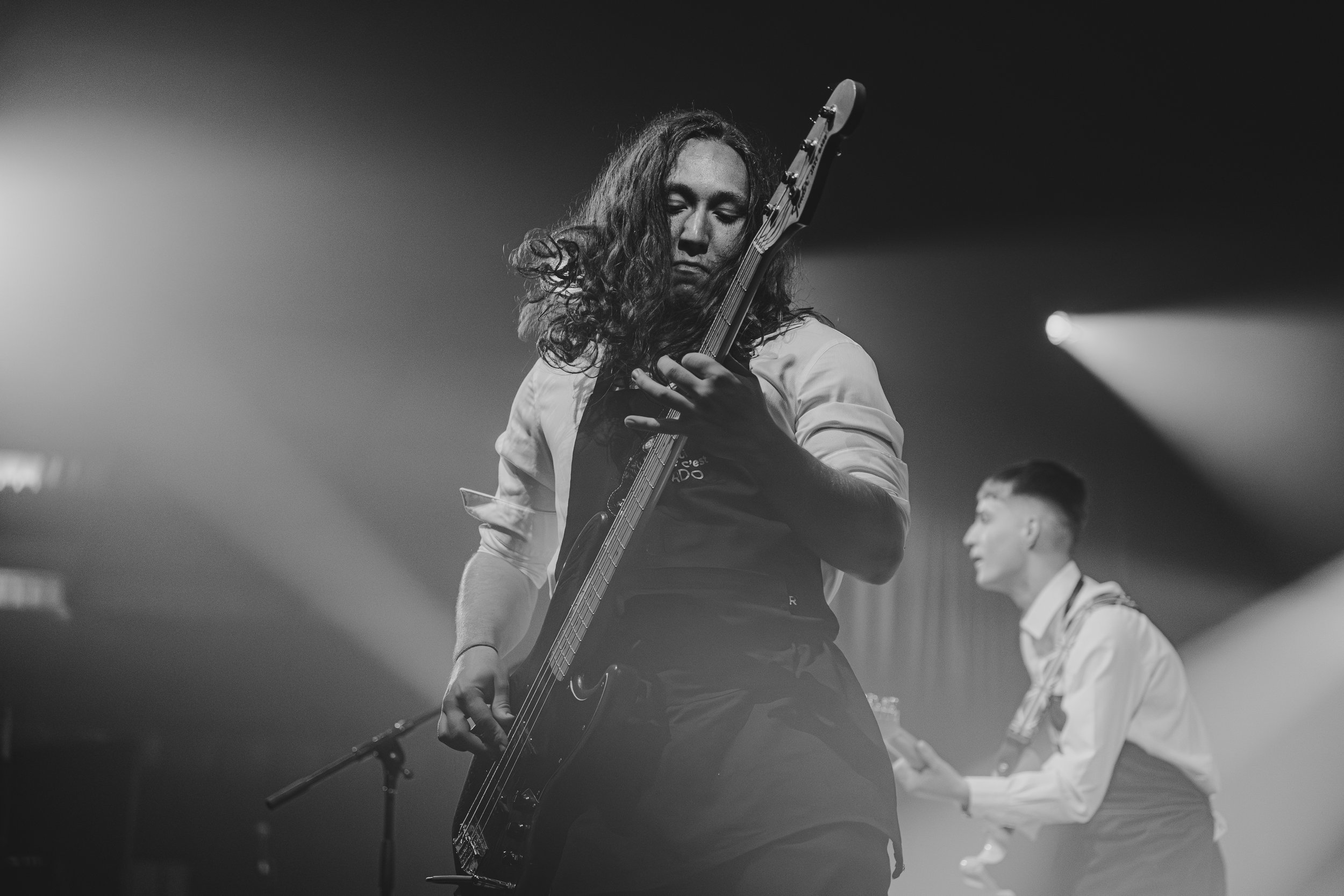 Deux musiciens jouent de la guitare électrique sur scène, en noir et blanc, avec un éclairage de scène.