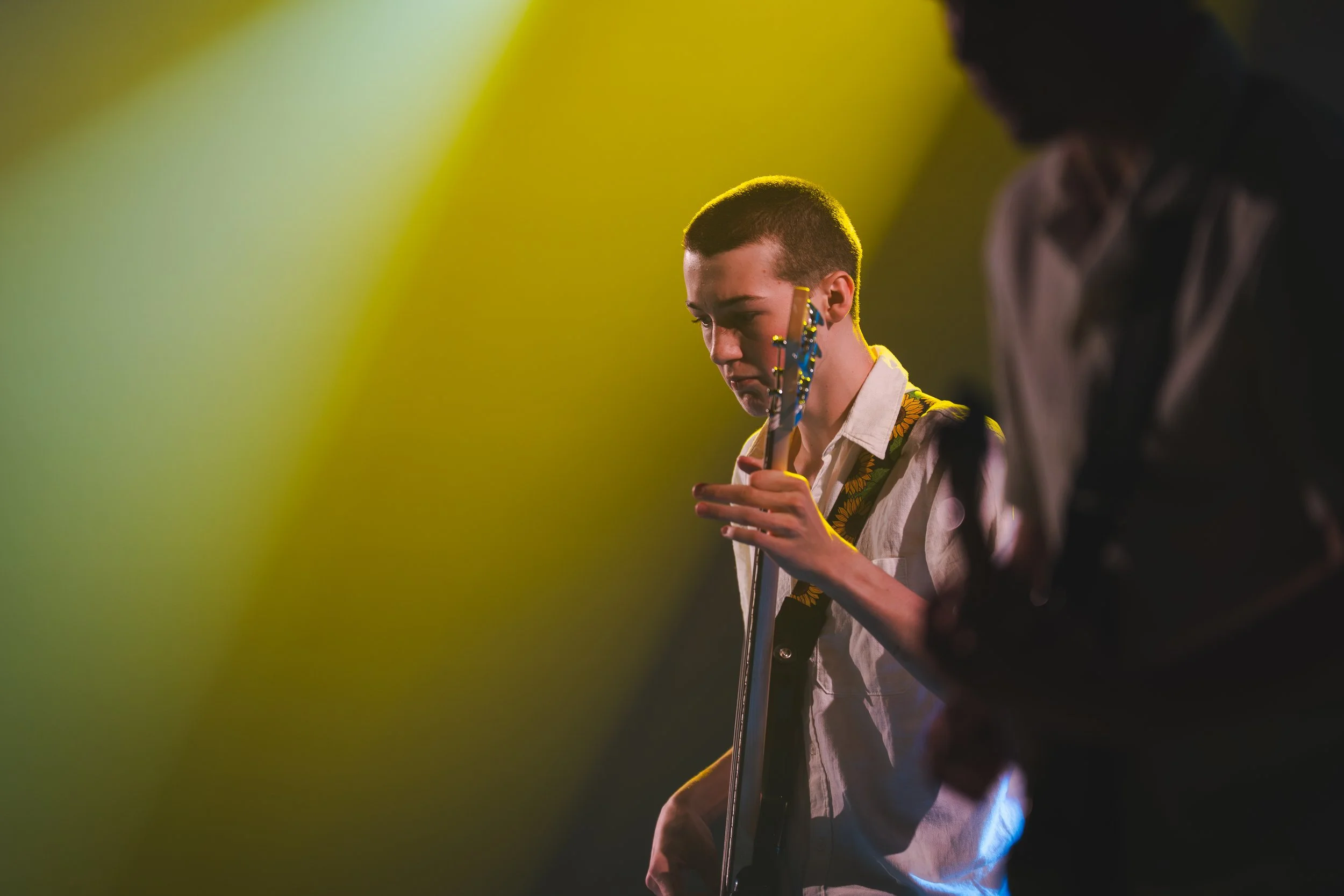 Jeune musicienne jouant de la guitare lors d'une performance sur scène, éclairée par un éclairage jaune