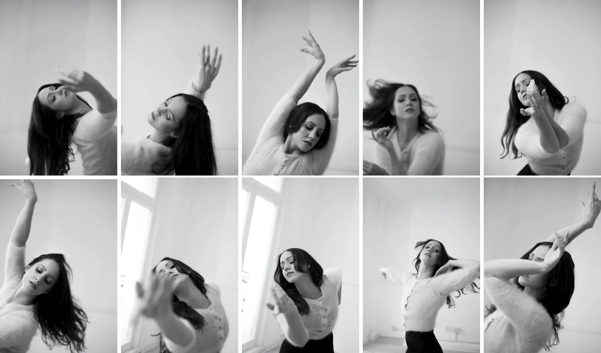 A woman with long dark hair in a white sweater and black pants is dancing and posing in a bright, minimal studio with large windows, captured in black and white.