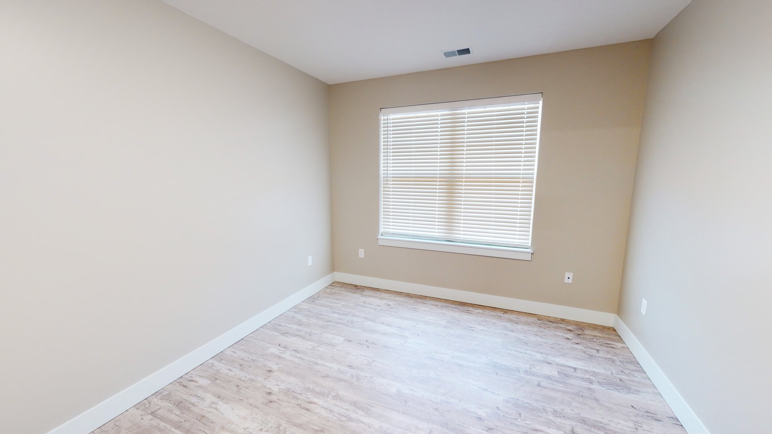 Empty room with beige walls, light wood floor, and a window with blinds.