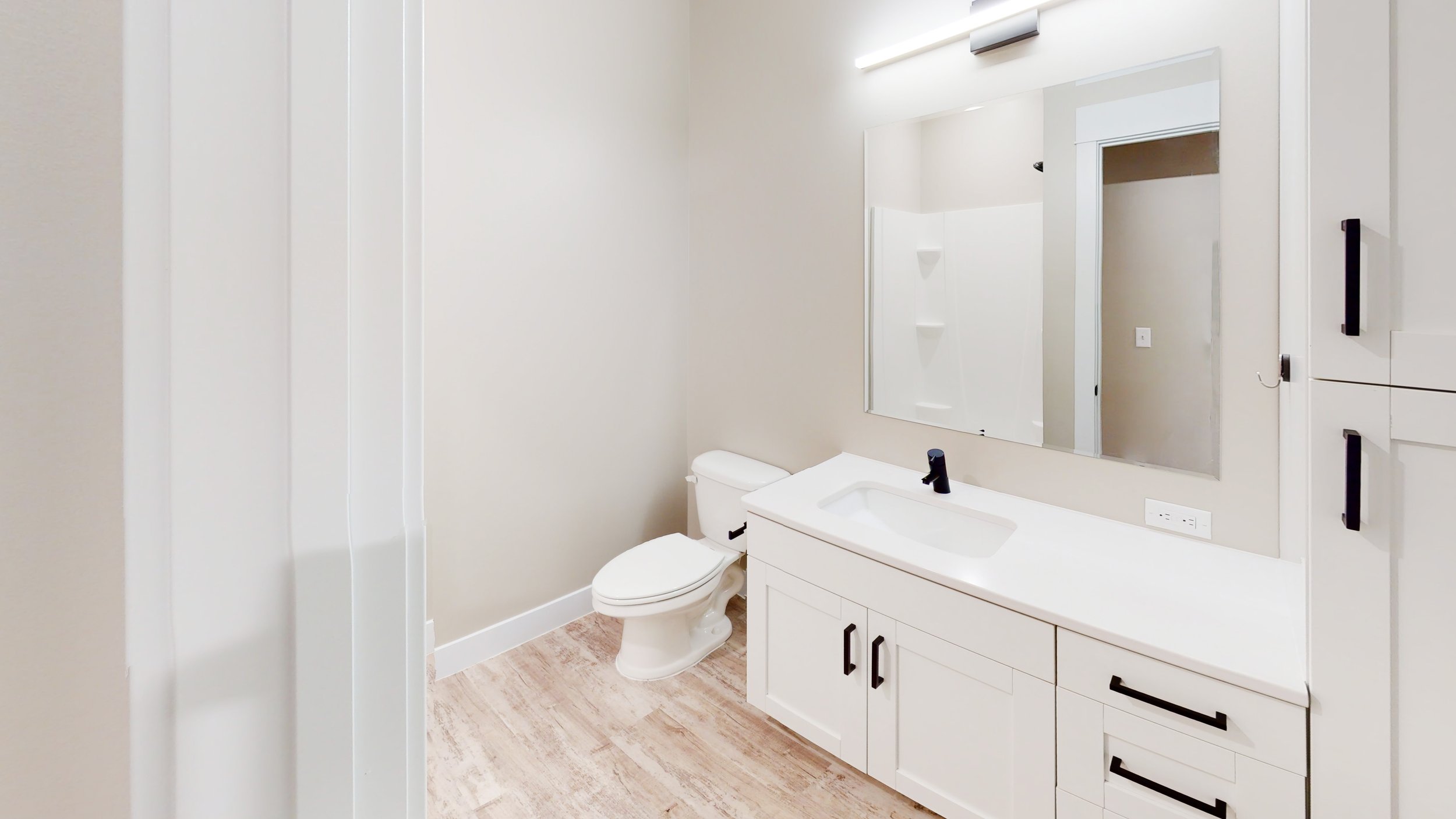 Modern bathroom with white vanity, large mirror, toilet, and light wood flooring.