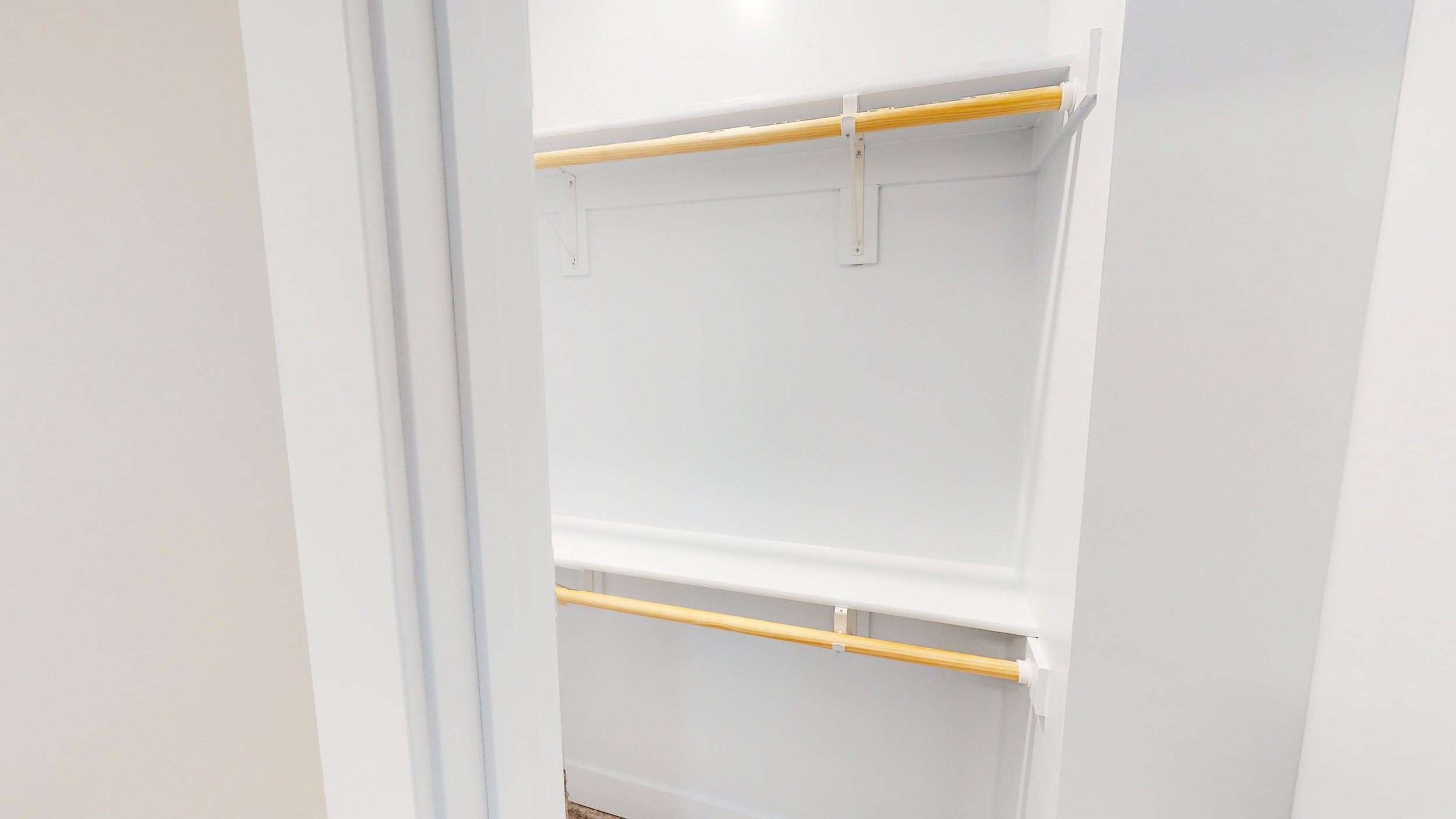 Empty white closet with wooden rods and shelving.