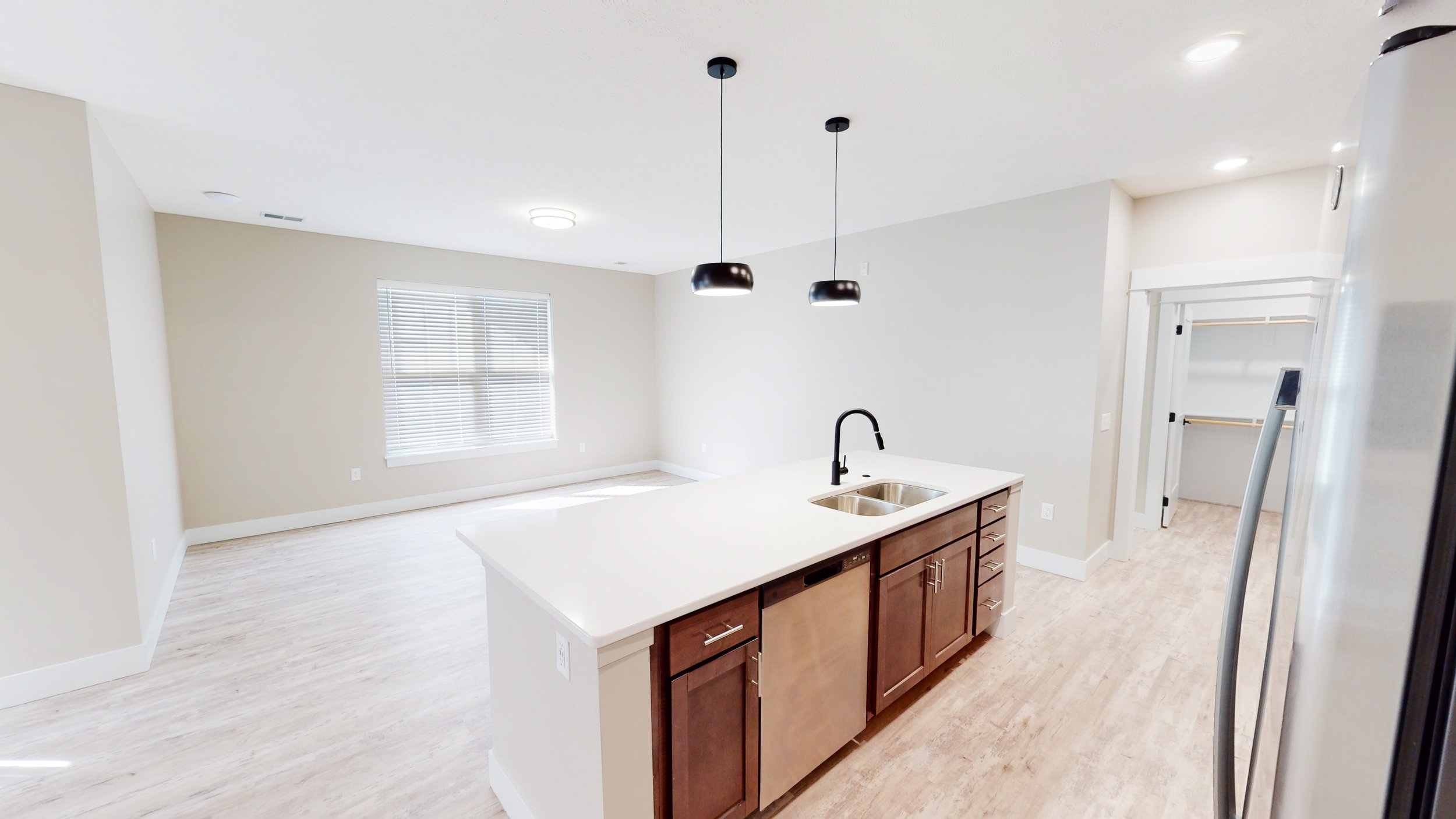 Modern kitchen with island, double sink, stainless steel appliances, pendant lights, and adjacent open living space with hardwood floors.
