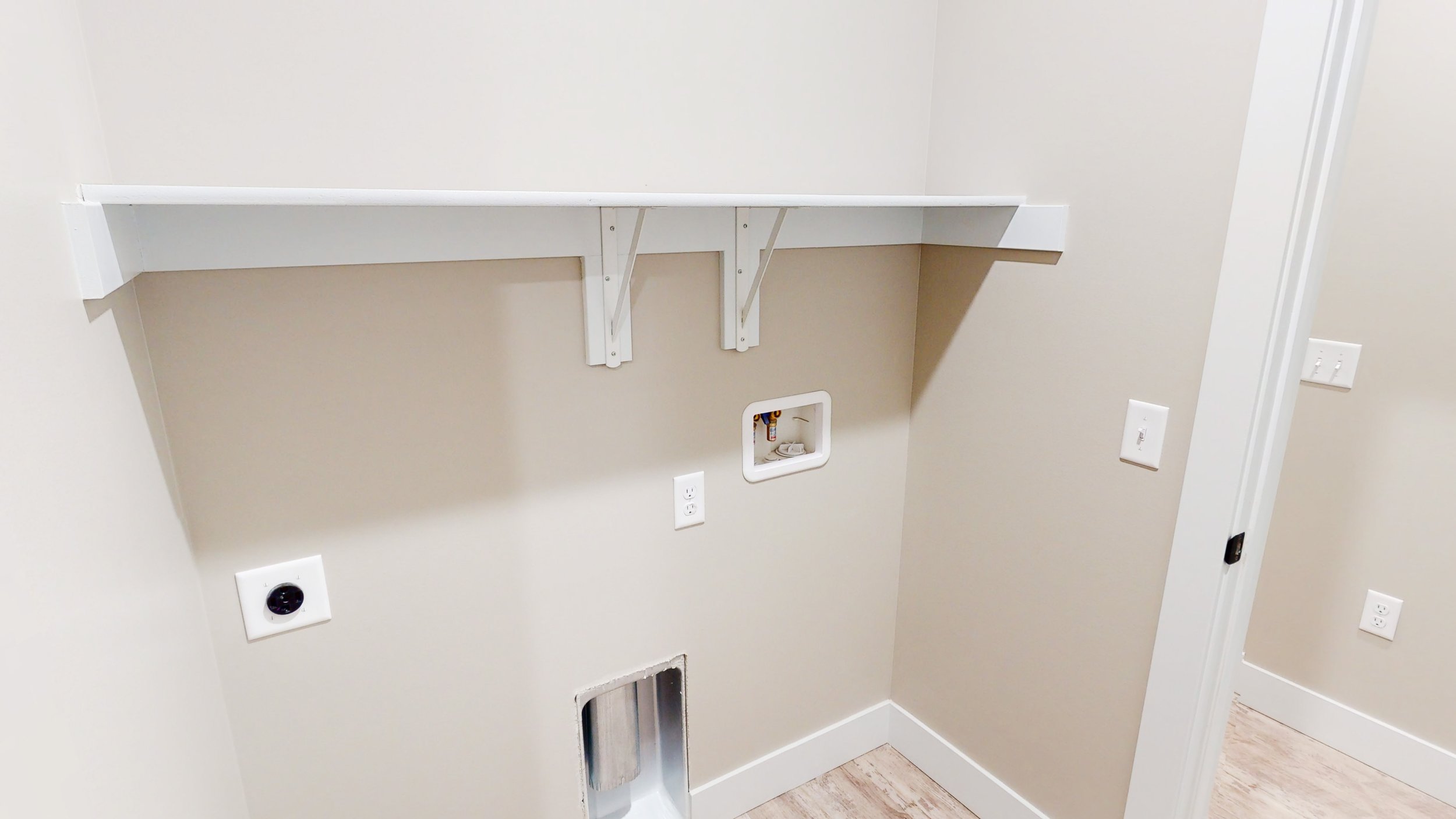 Laundry room with hookups for washer and dryer, wall shelf, and electrical outlets.
