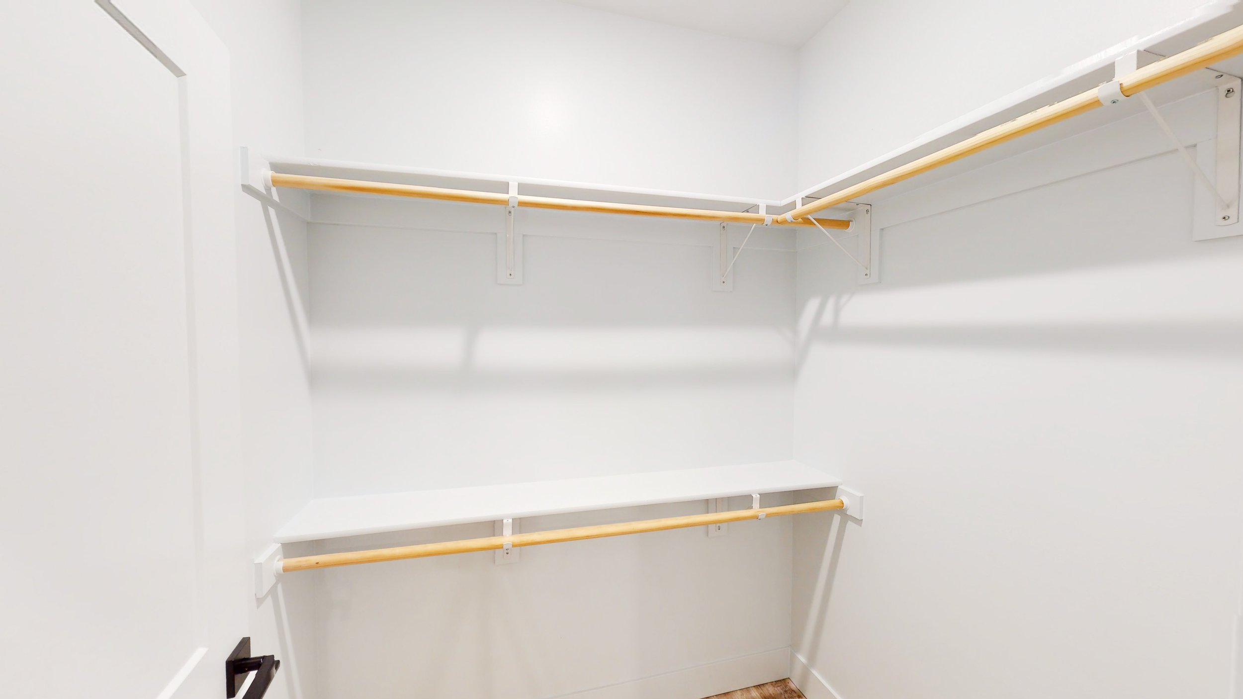 Empty walk-in closet with white walls and wooden clothing rods.